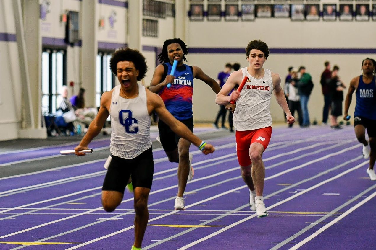Athletes racing on indoor track during competitive running event.