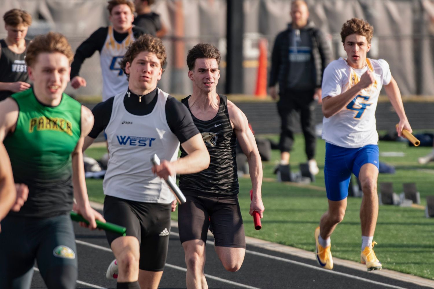 High school relay runners competing on a track, passing a baton during a sprint race event.