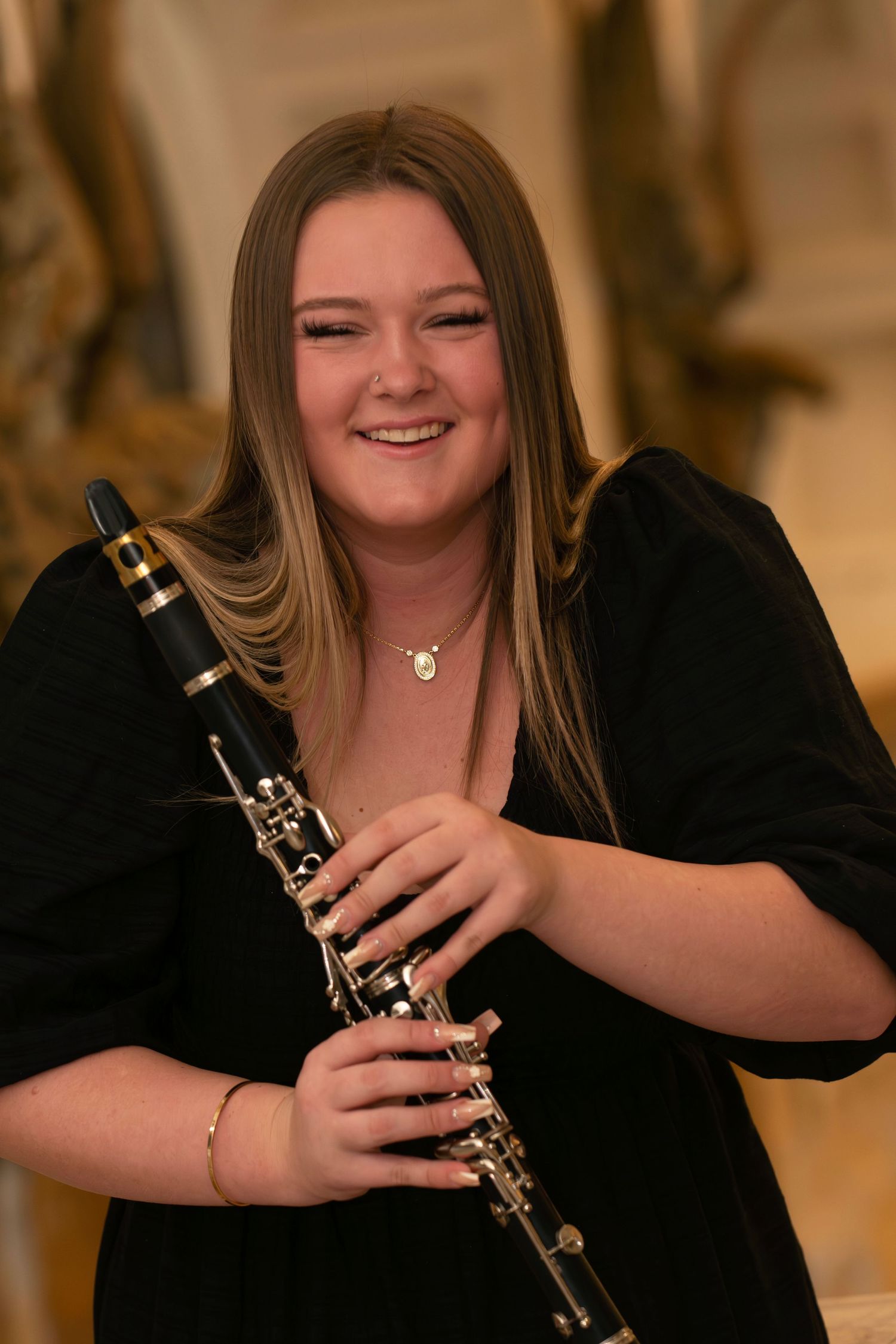 A musician in a black top smiles while holding a clarinet during a performance.