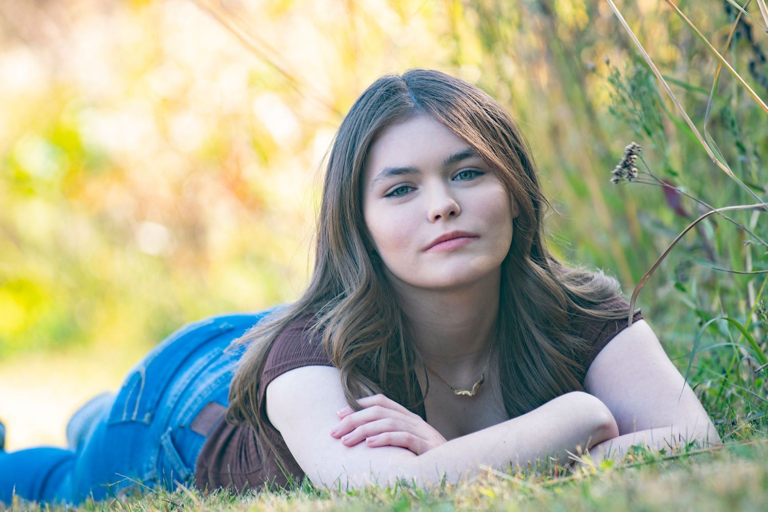 Casual pose outdoors with someone lying on grass in natural lighting for her Senior Essentials portrait session with Simply Junique.