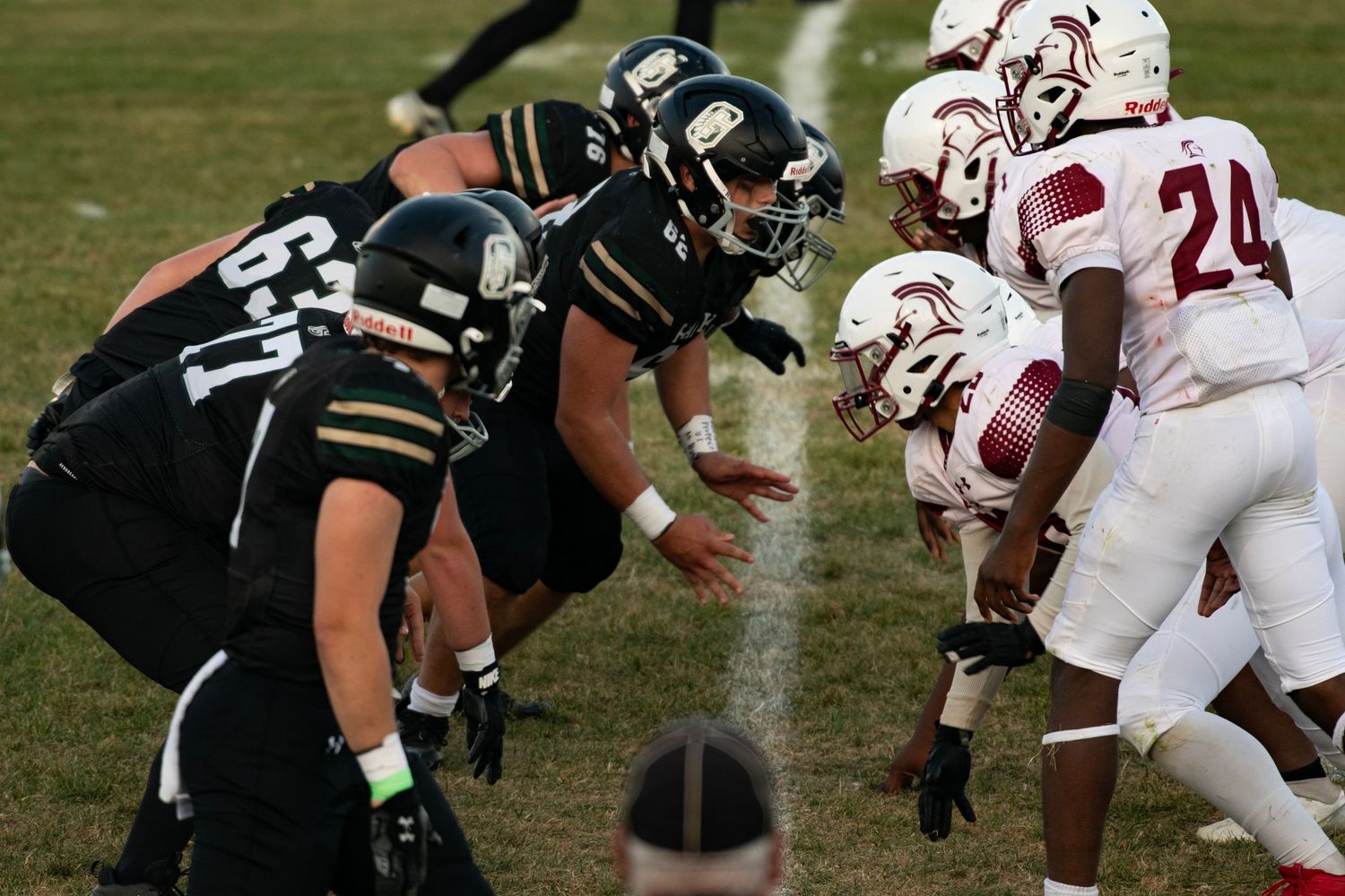 Football players line up at scrimmage, black uniforms vs. red and white, during an intense high school football game.