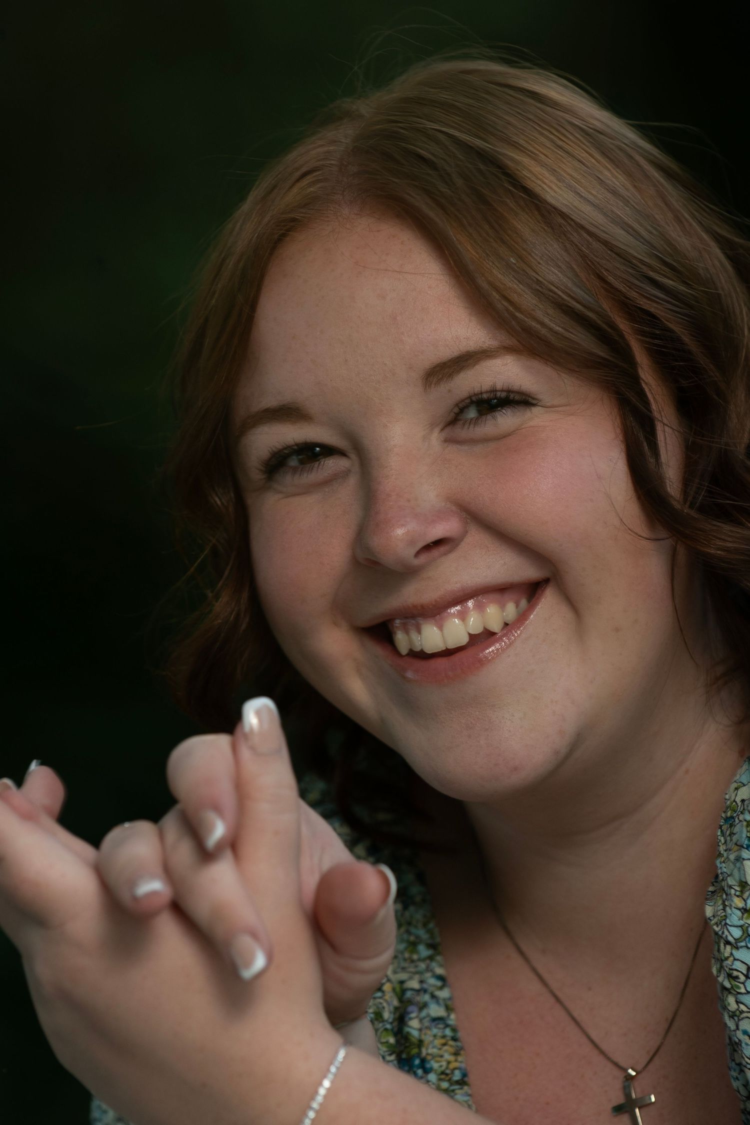 Smiling young woman with red hair clapping her hands, wearing a necklace and bracelet outdoors.