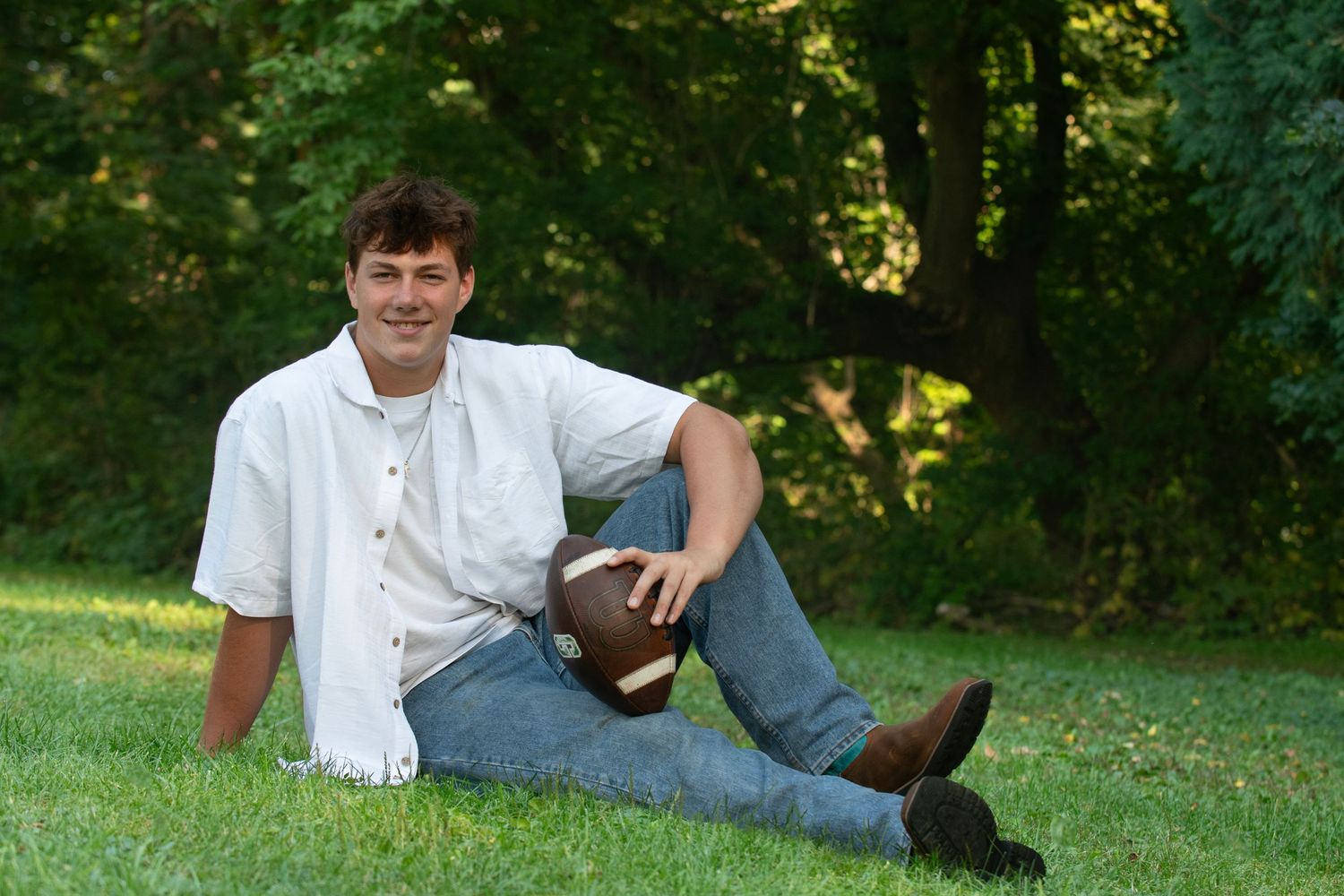 Person in casual attire relaxing on green grass in summer park setting during golden hour.