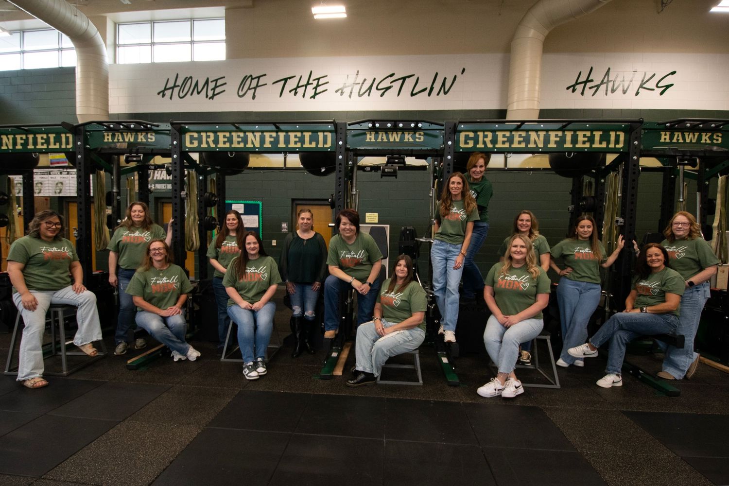 Group of people sitting in a row against a wall at a gym with 'Home of the Horton' signage visible.