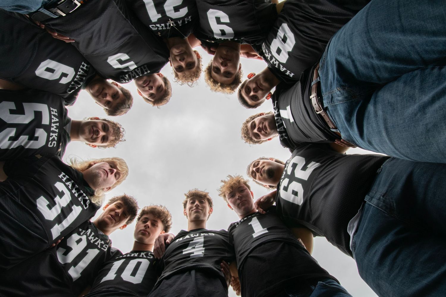 Team huddle viewed from below, players in black jerseys forming a circle against a bright sky.