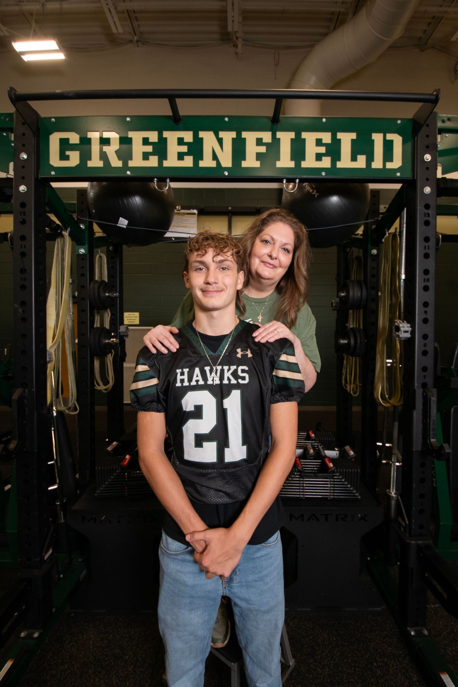 Students pose in athletic training room wearing Hawks jerseys and casual clothing at Greenfield school facility.