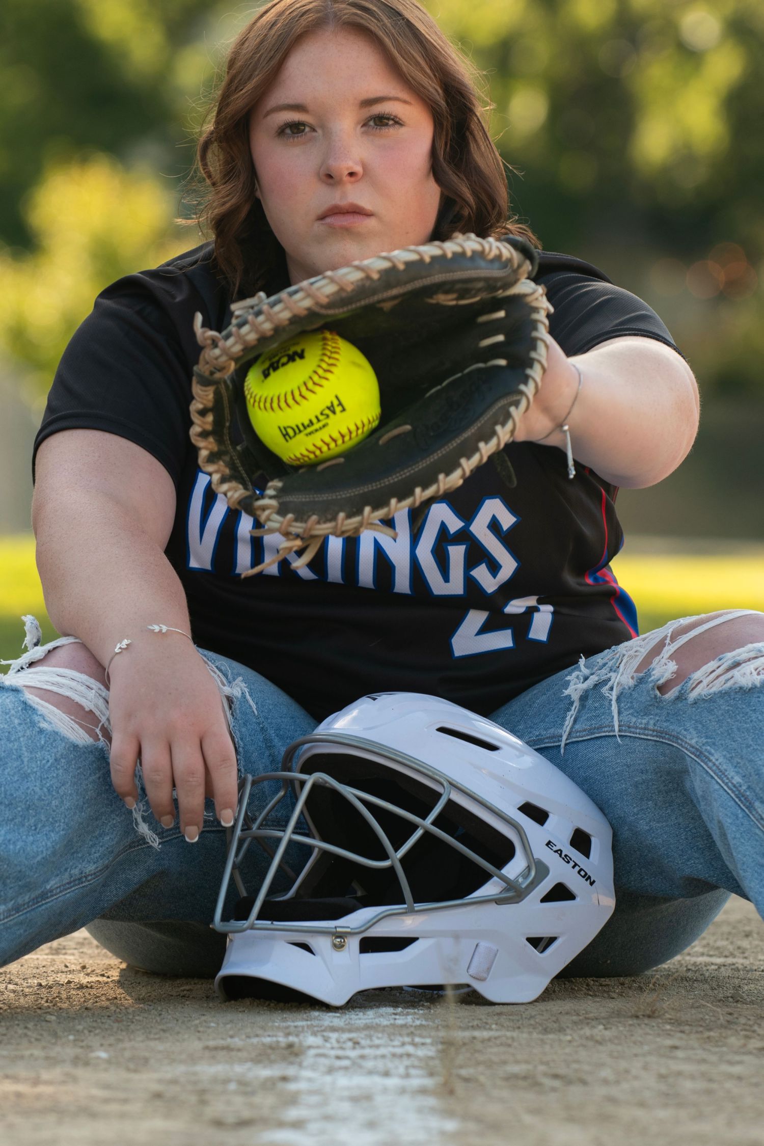 Creative softball player poses with yellow ball, glove, and helmet while wearing Vikings team jersey during sports photoshoot.