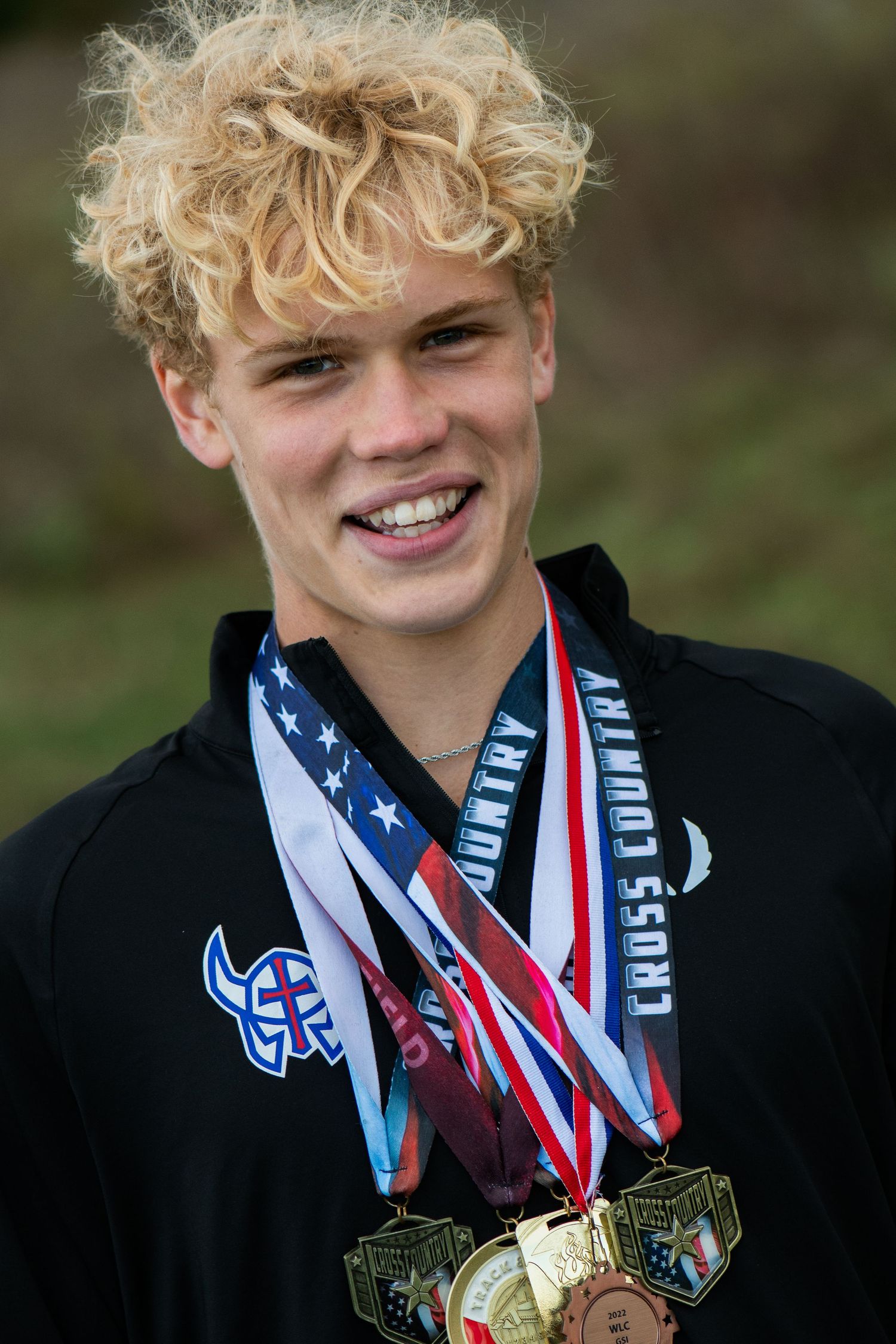 Athletic achievement display with multiple medals and awards worn around neck against dark background. Milwaukee County Grounds