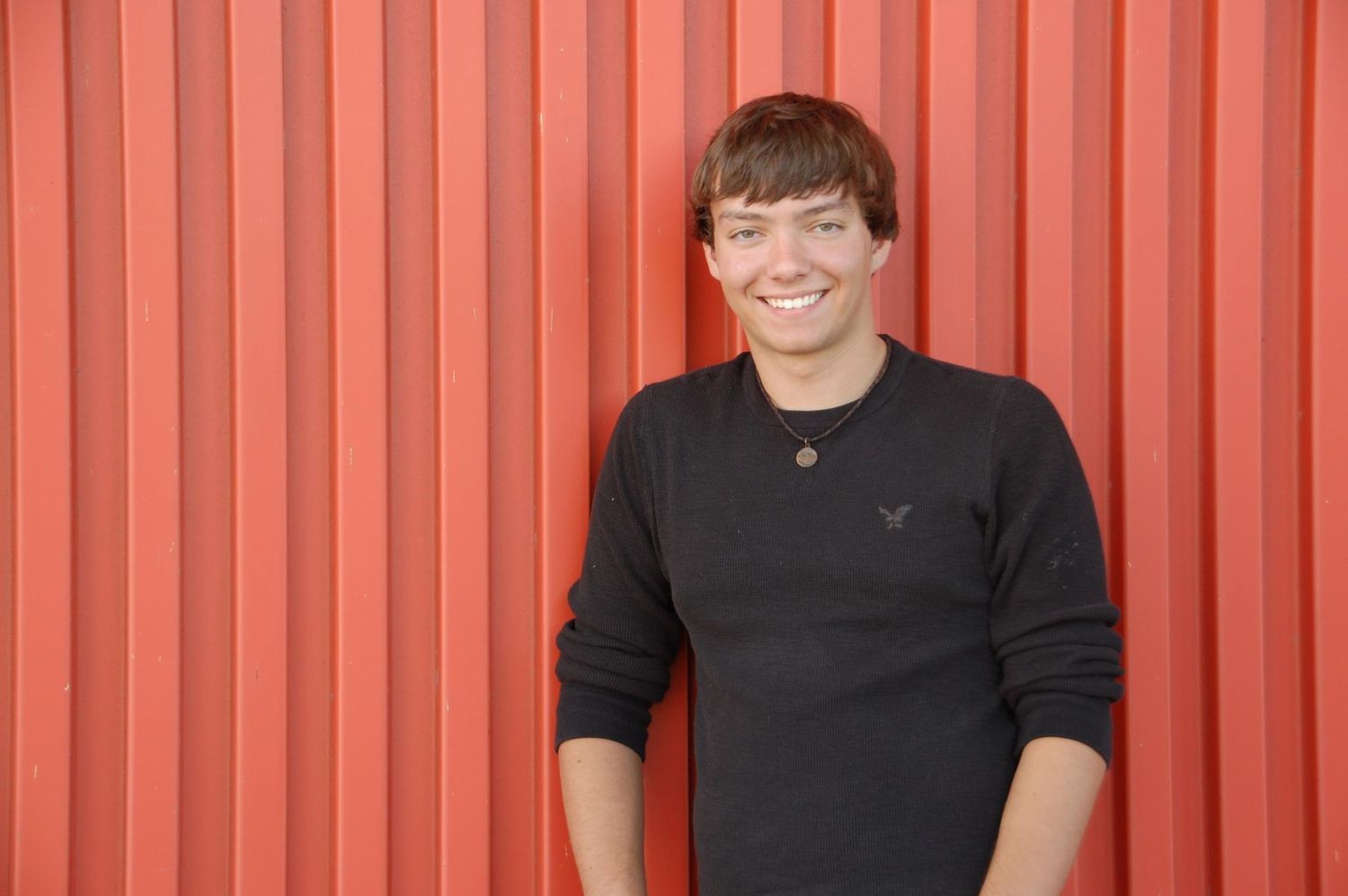 Casual high school senior portrait against orange corrugated metal background at the Harley Davidson Museum in Milwaukee, WI