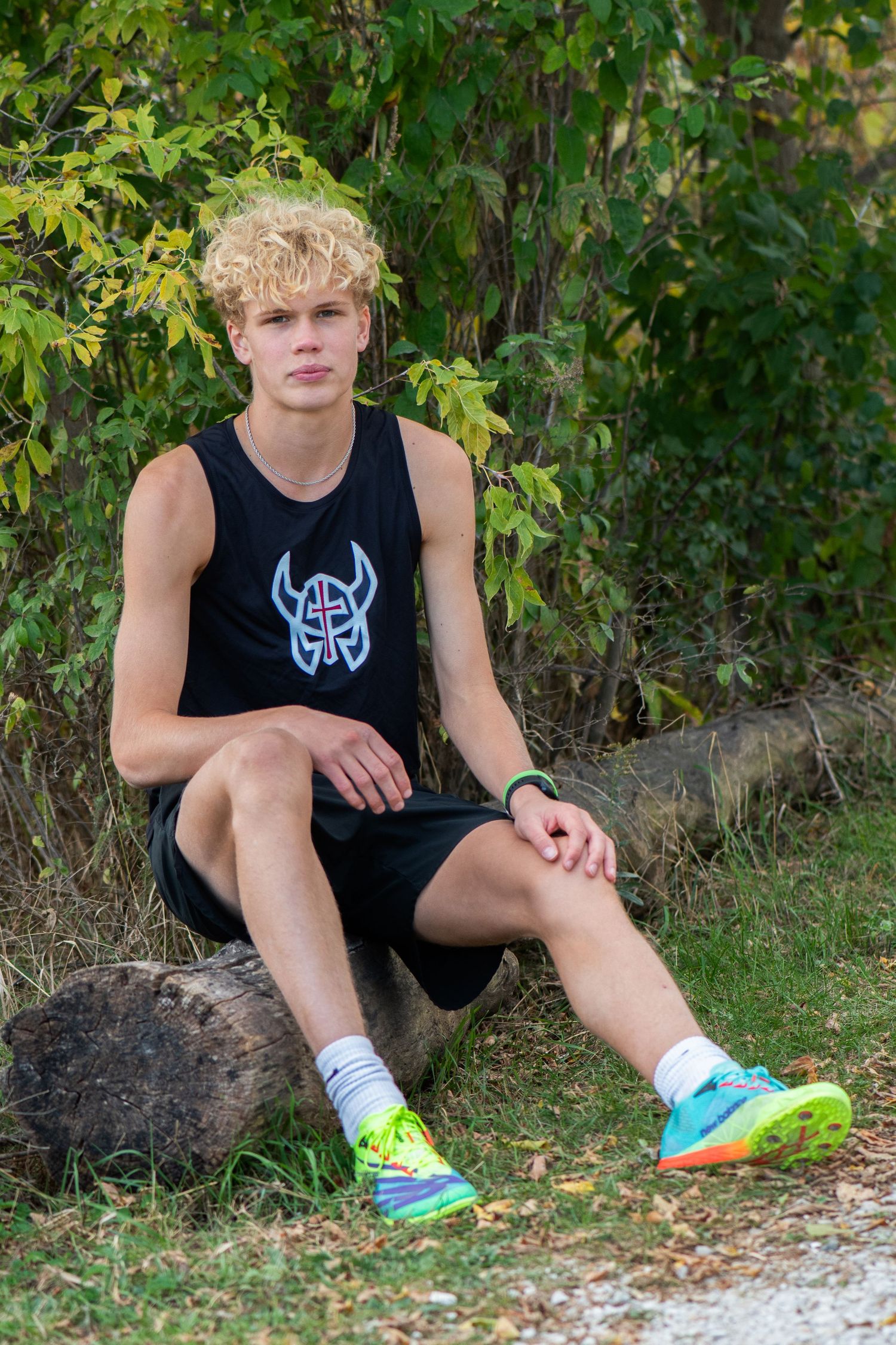 Person resting on fallen tree trunk wearing black athletic tank and mismatched neon sneakers in natural outdoor setting. Milwaukee County