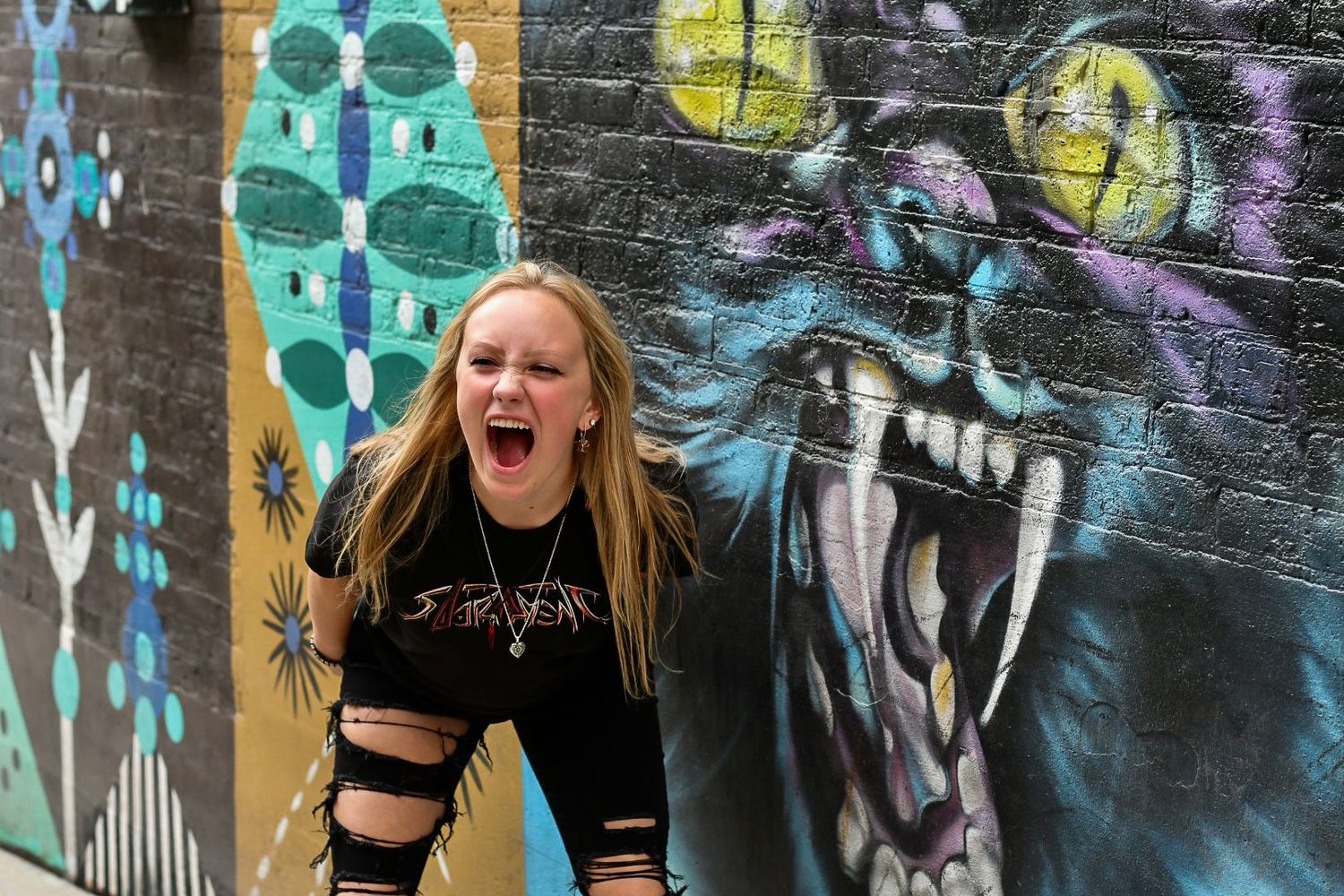 Creative poses in front of vibrant graffiti wall with colorful abstract designs.