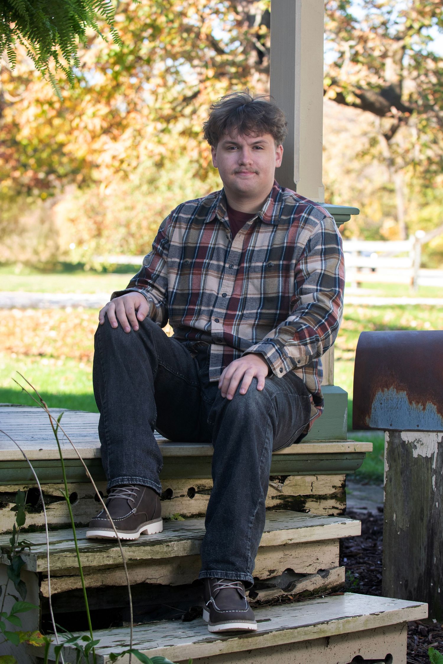 Young man in plaid shirt sitting on wooden steps outdoors in autumn.