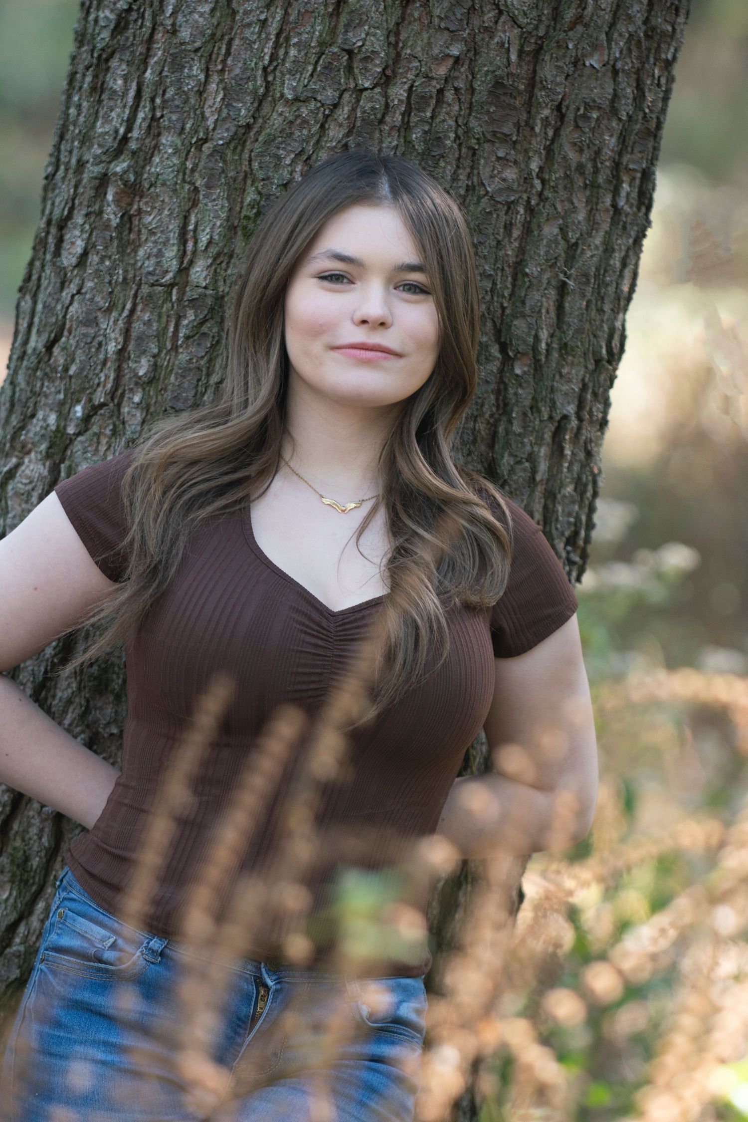 Portrait sequence against tree trunk showing casual poses in brown top and blue jeans.