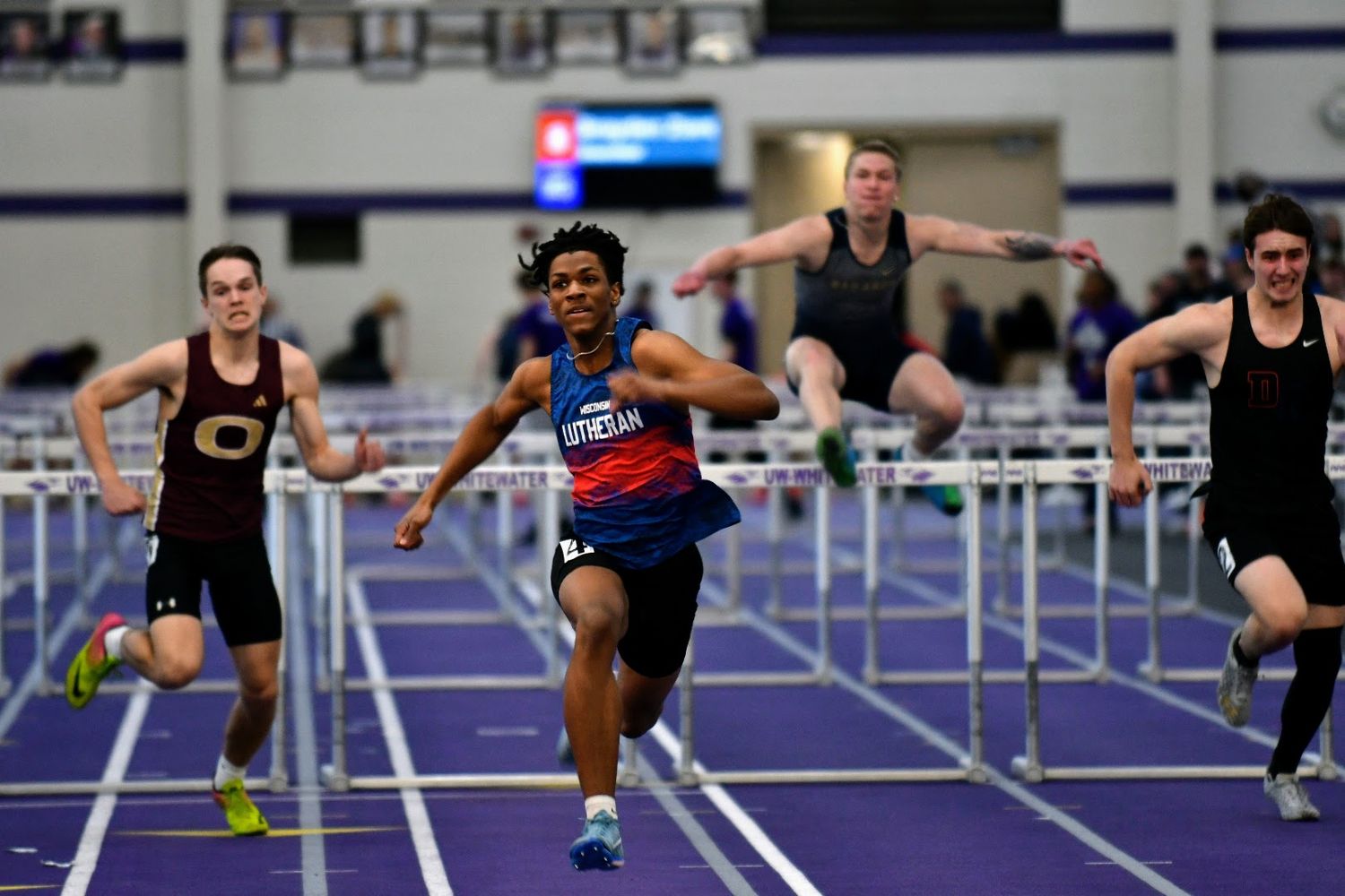 Row of athletes competing in hurdle race on indoor track. Game Day to Grad Day Senior Portrait Experience. Simply Junique