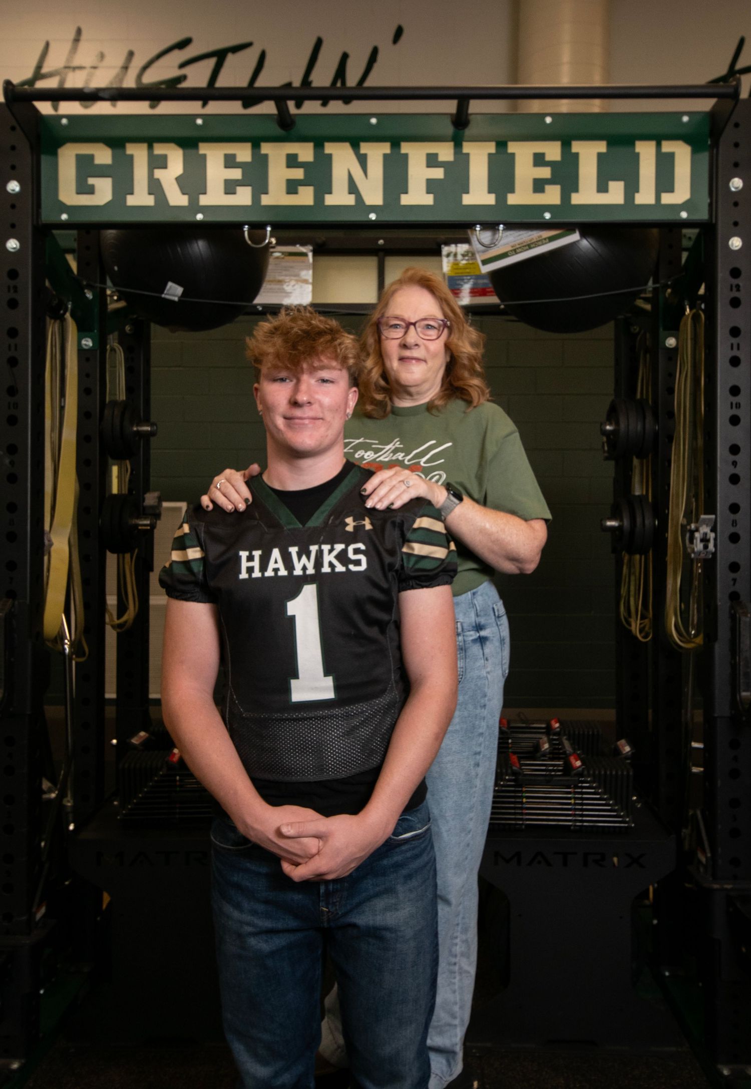 A group of people wearing dark clothing pose in front of a gym wall with 'GREENFIELD' signage.