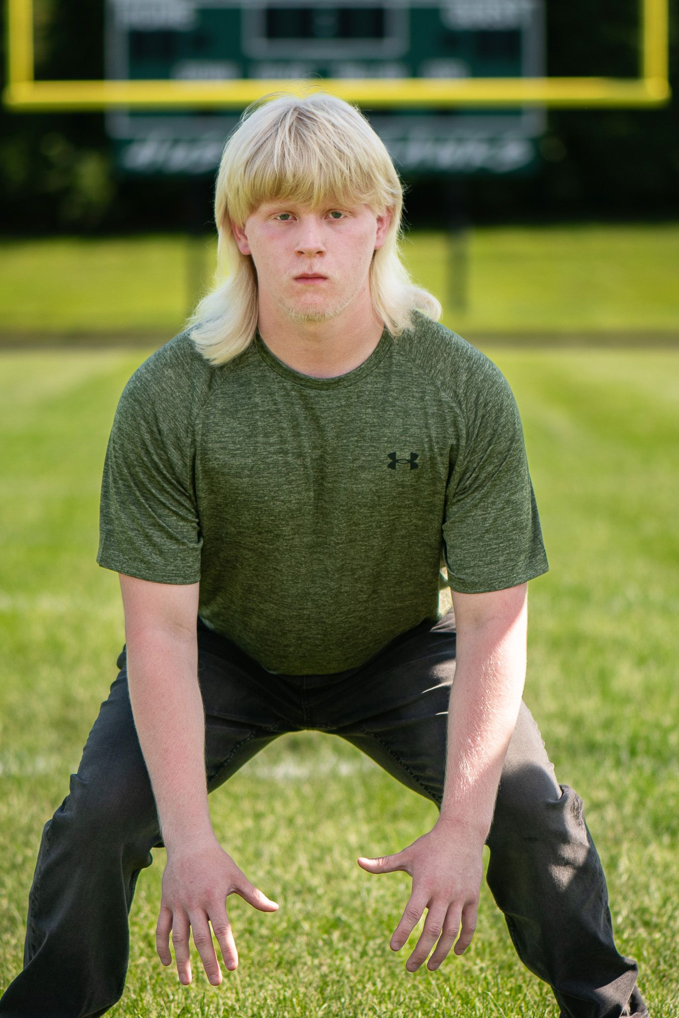 A person in athletic wear demonstrates football stance positions on a green playing field. Game Day to Grad Day Senior Portrait Experience