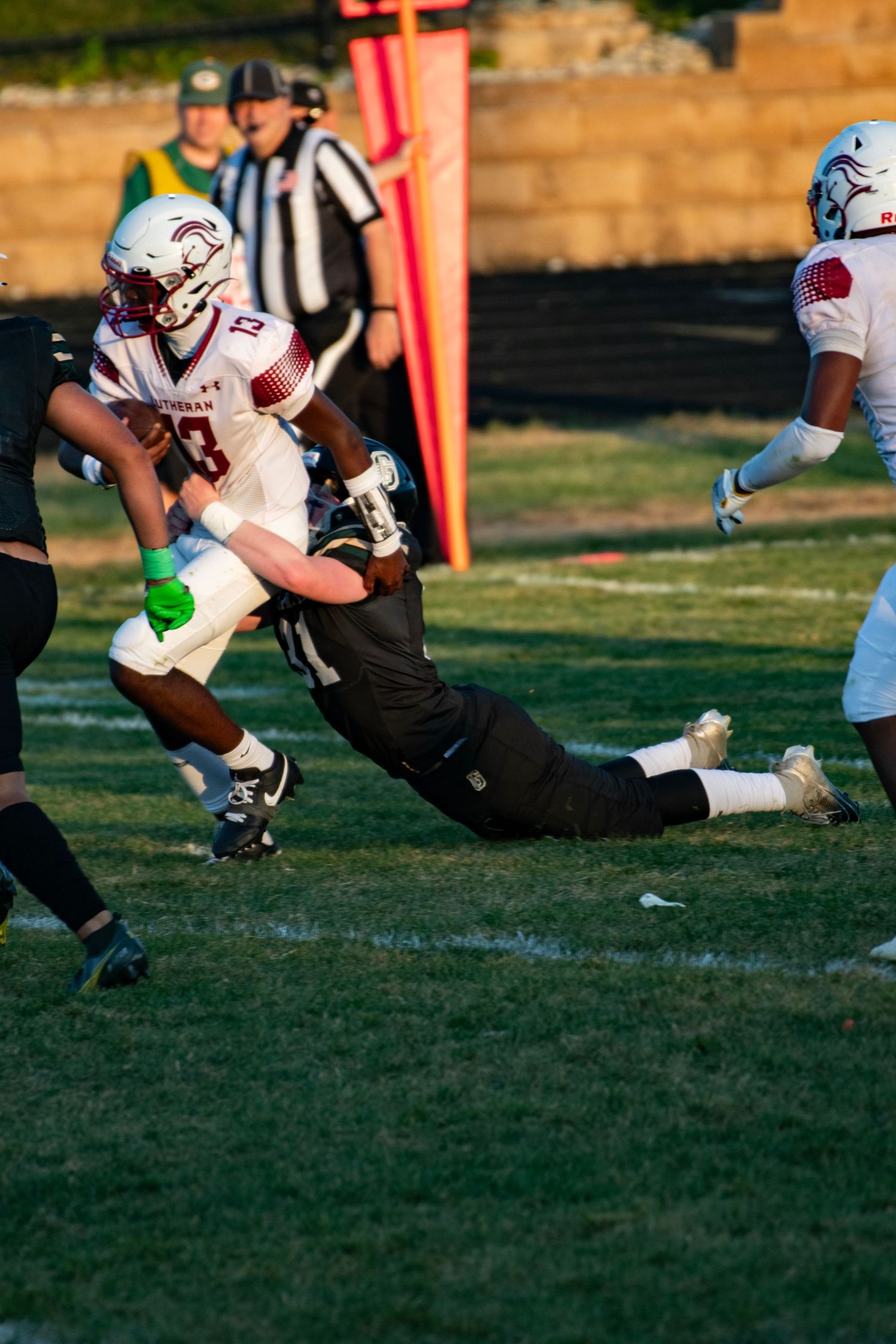 Football player in black uniform makes diving tackle on opponent during high school game.