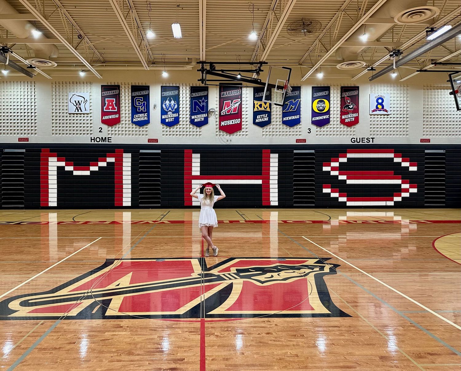 Modern high school gymnasium with polished wood floors and black and red wall graphics.