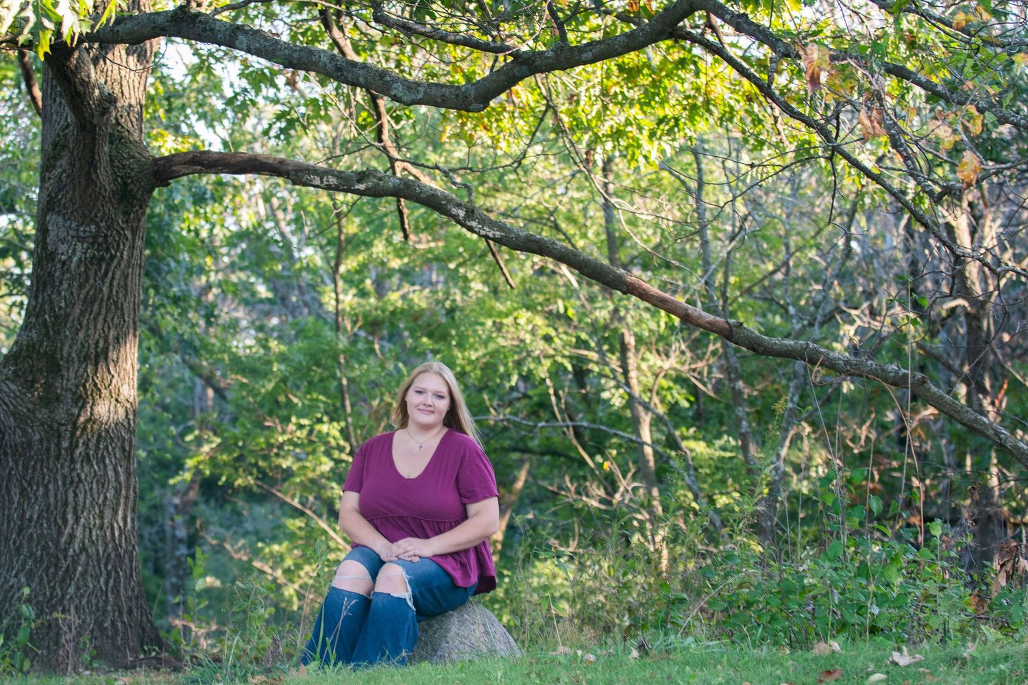 A lush wooded outdoor portrait setting with green trees and dappled sunlight creating a natural backdrop.