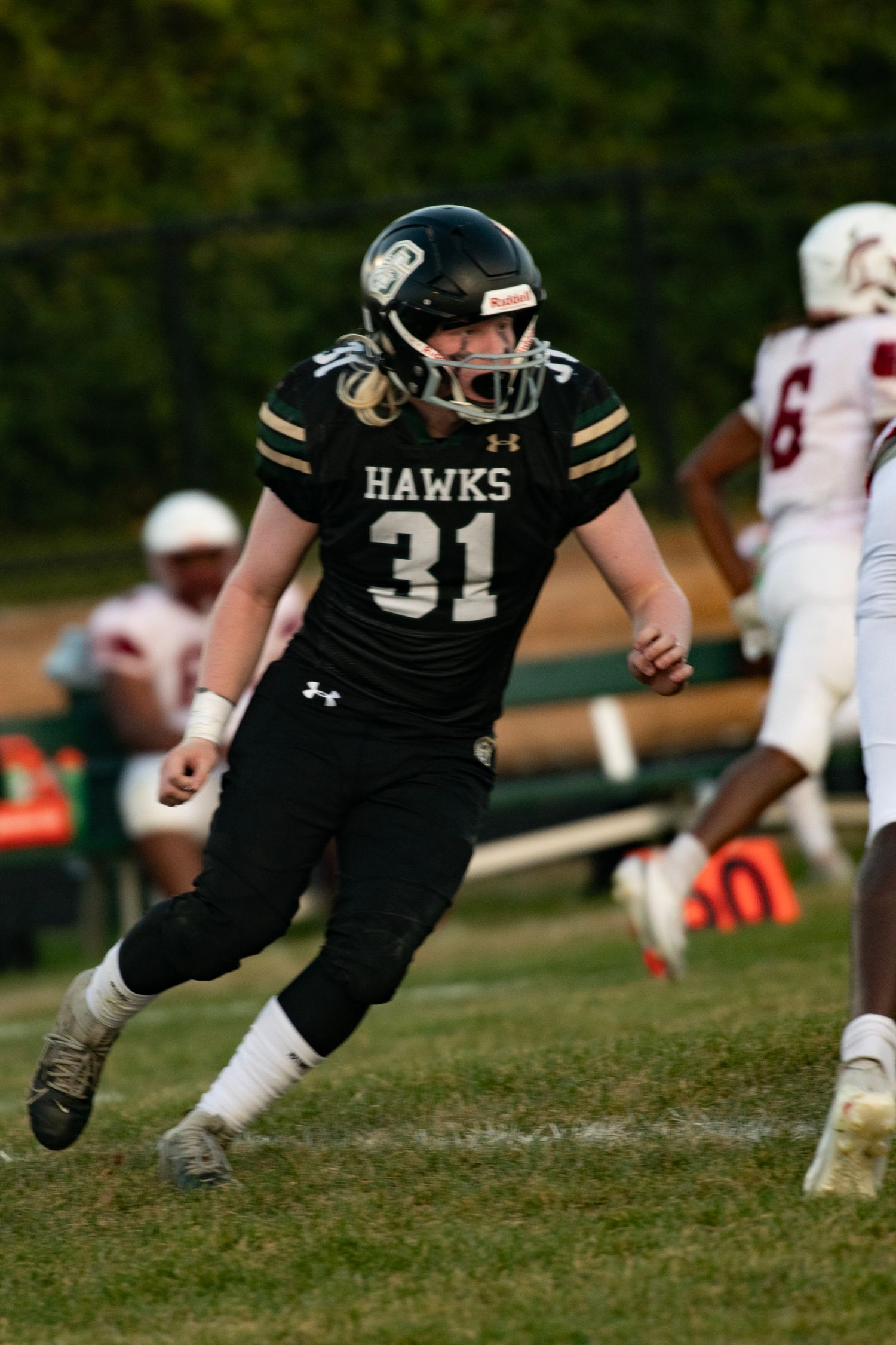 Hawks #31 football player in black uniform sprints on field during high school game.