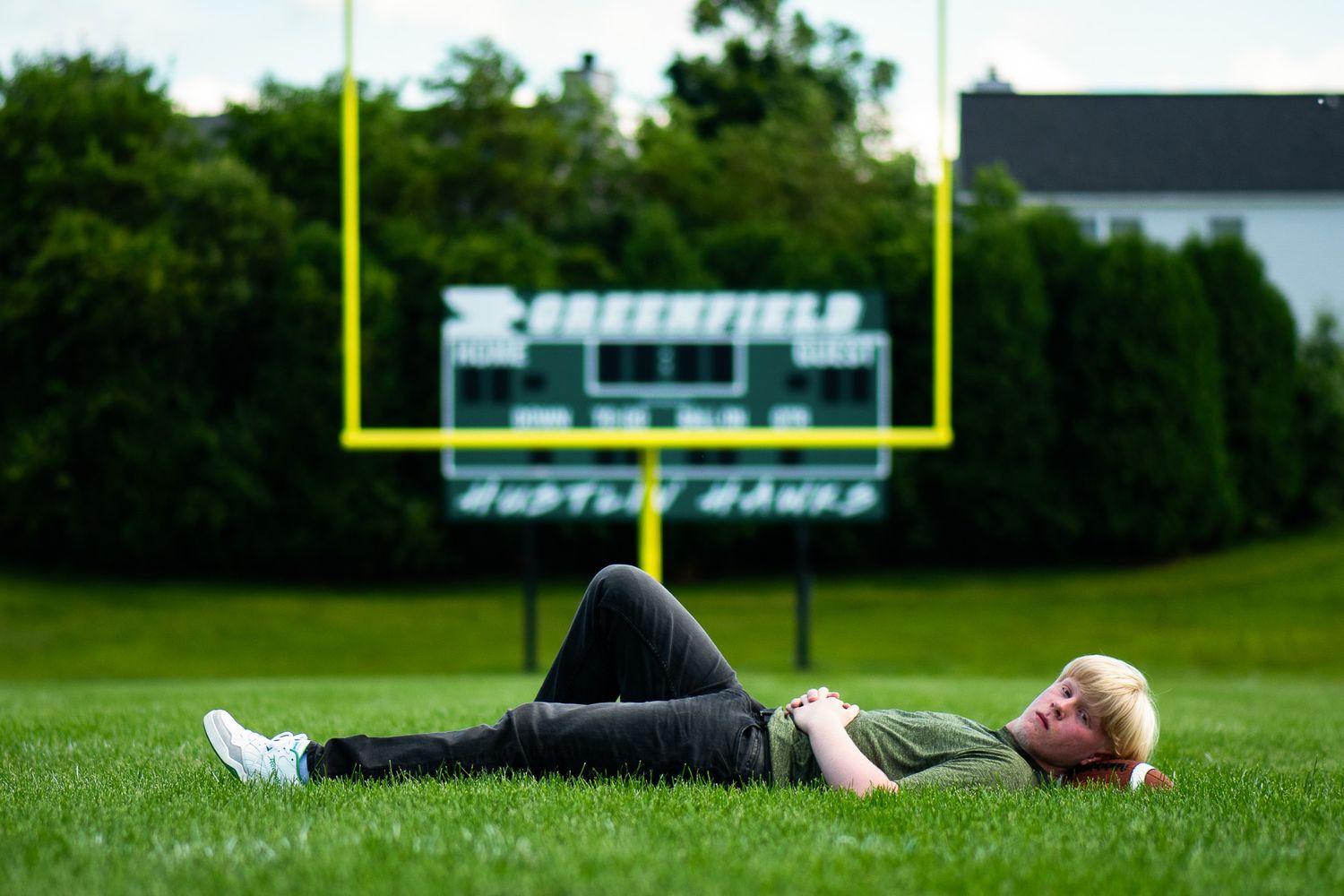 A wide shot of a football field shows goal posts and athletic facilities in the background. Game Day to Grad Day Senior Portrait Experience