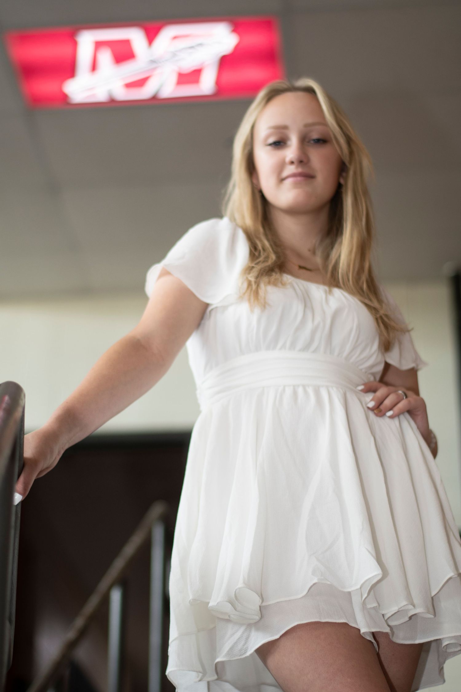 Person in flowy white dress twirls and poses in indoor setting with red signage visible.
