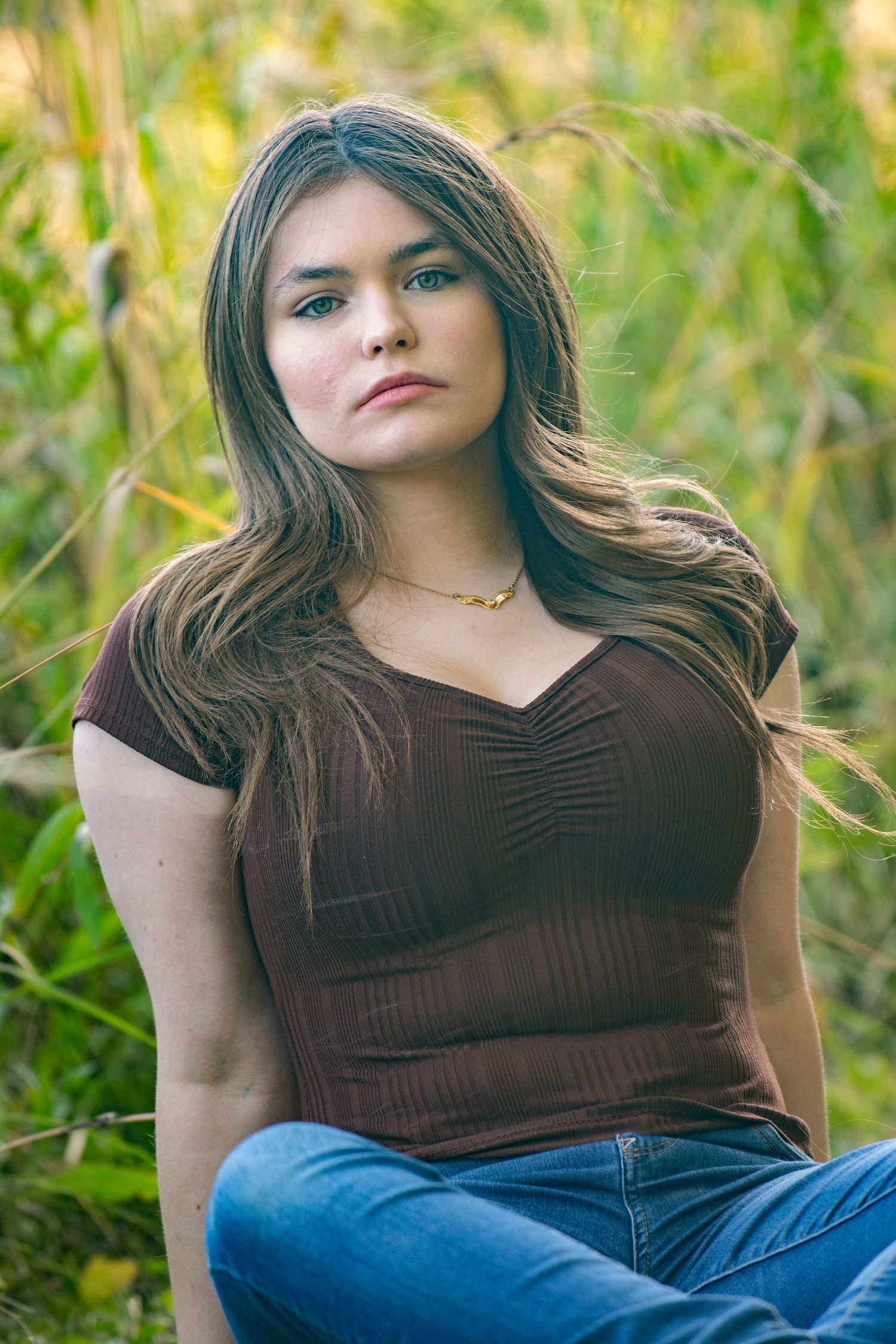 Female high school senior poses outdoors against a natural green background with soft bokeh lighting for Simply Junique.