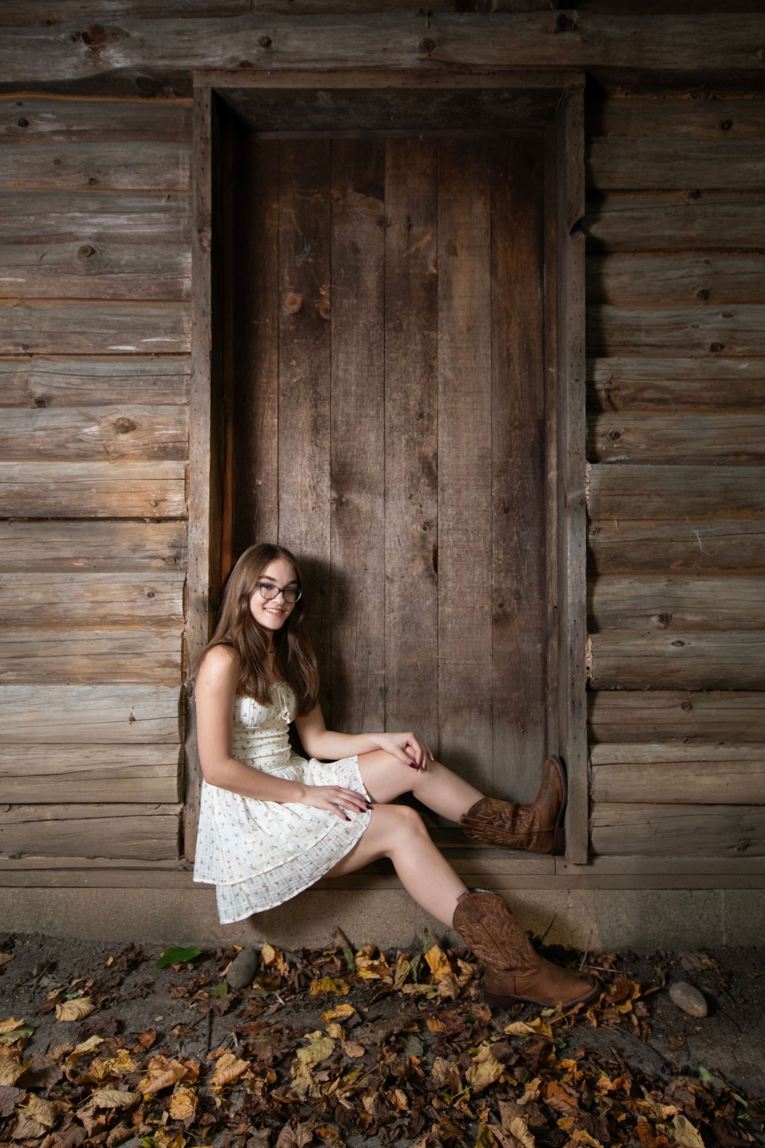 A rustic wooden barn wall with fallen autumn leaves creates a moody backdrop for a photoshoot scene.