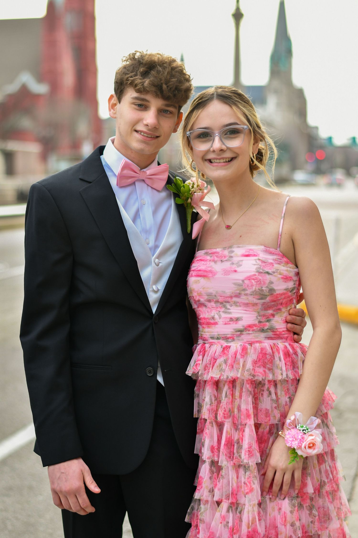 A young couple dressed for prom, boy in black tux with pink bow tie, girl in pink floral dress with wrist corsage.