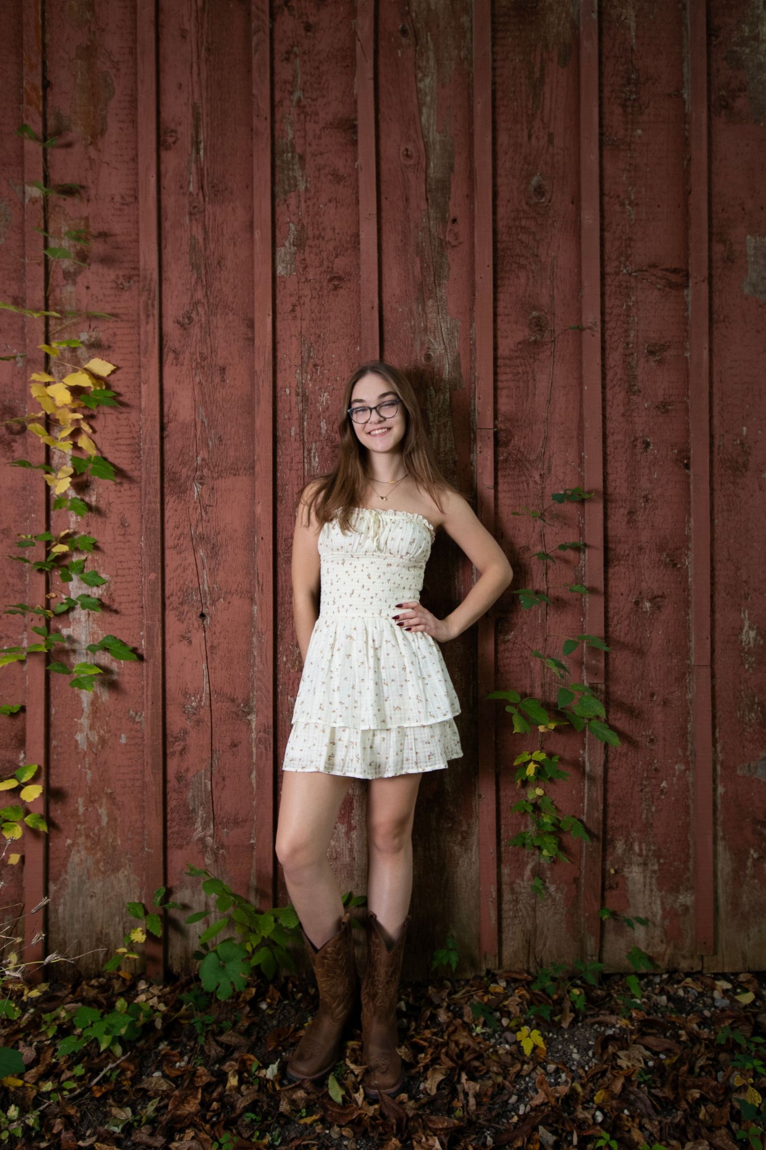 A series of four photos showing someone in a white dress posing against a rustic red barn wall with green foliage.