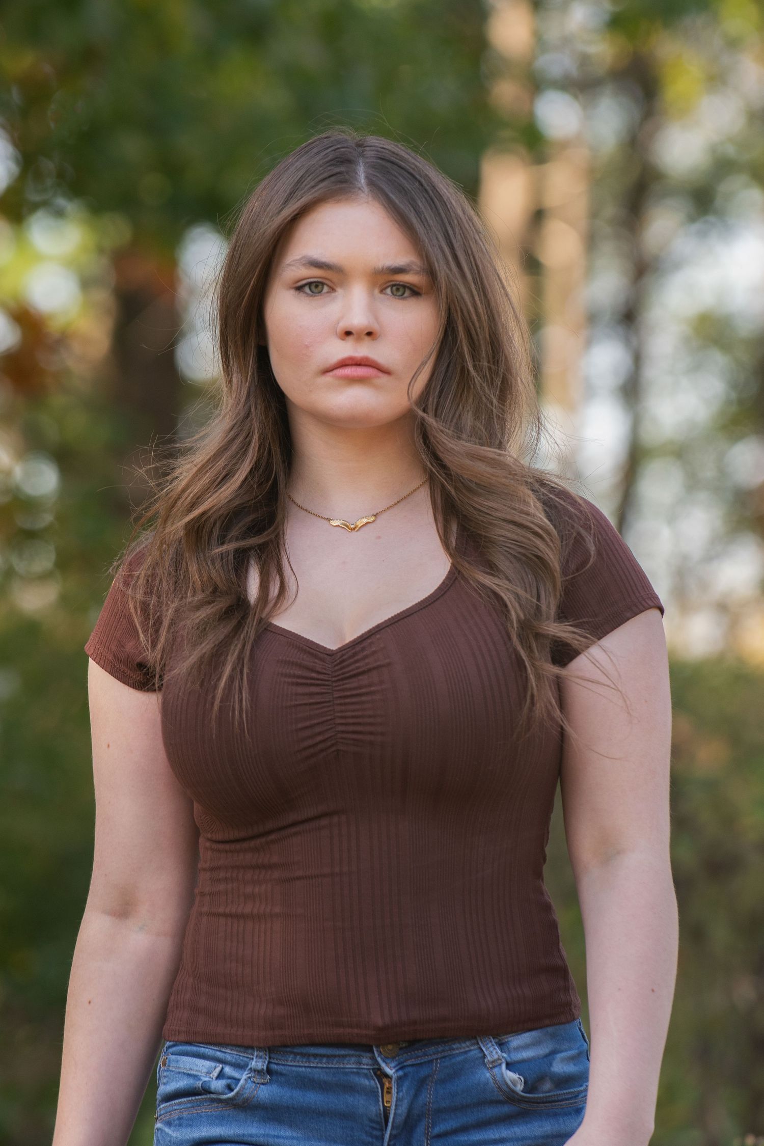 Fashion portrait series in brown v-neck top and jeans with natural outdoor background.