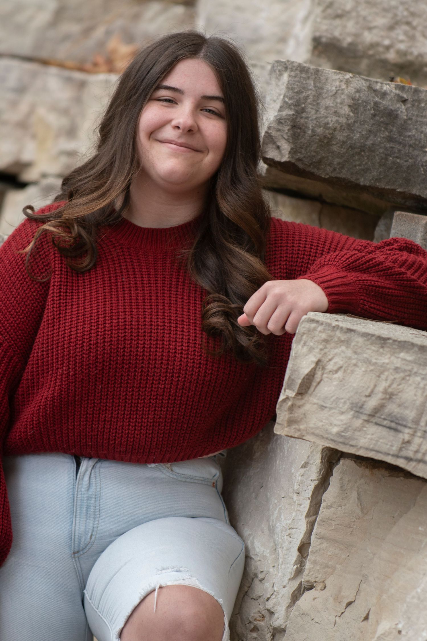 Portrait series against stone wall wearing red knit sweater in natural lighting.