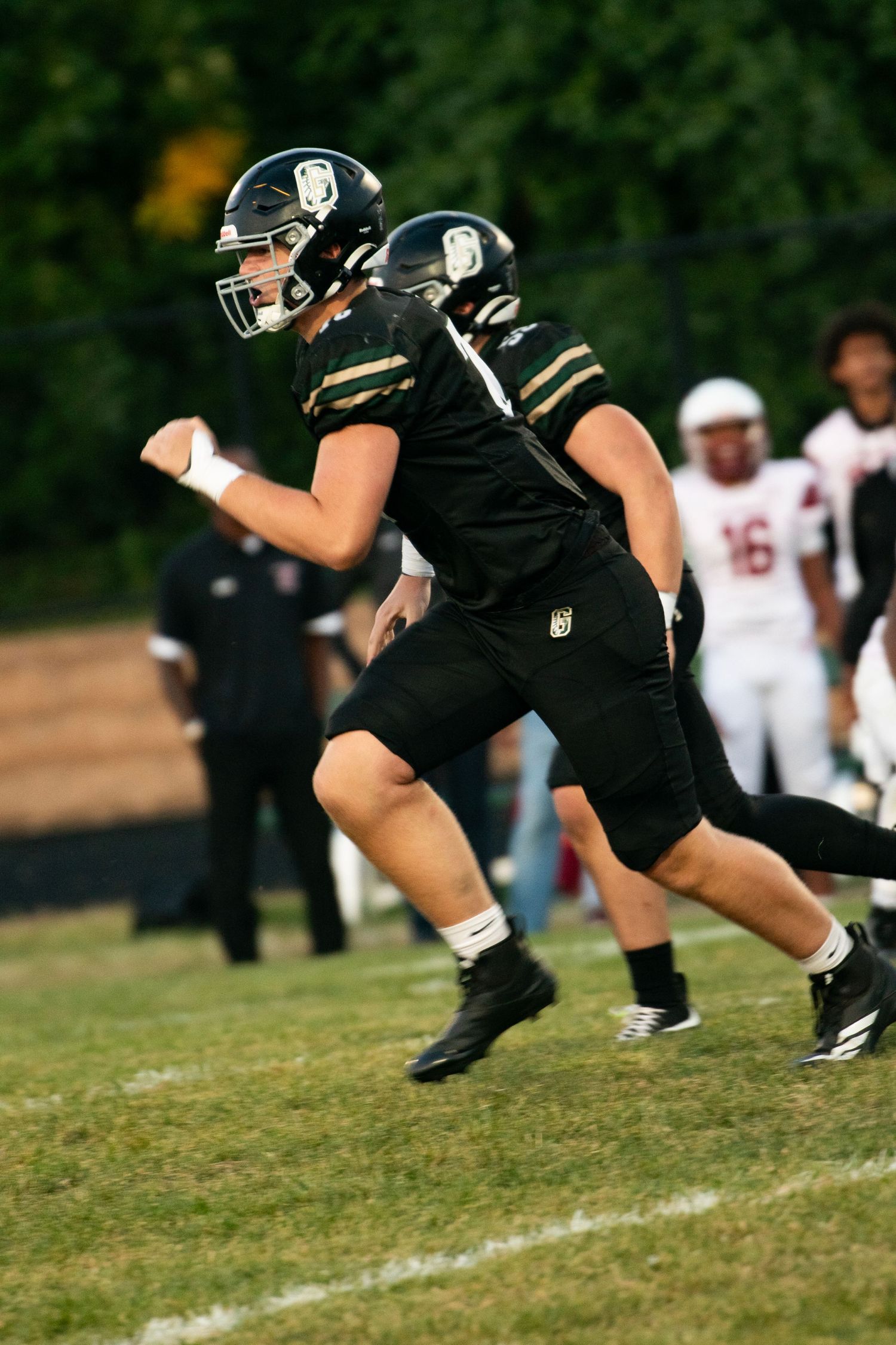 Football player wearing black uniform leans forward in dynamic kicking motion on grass field.