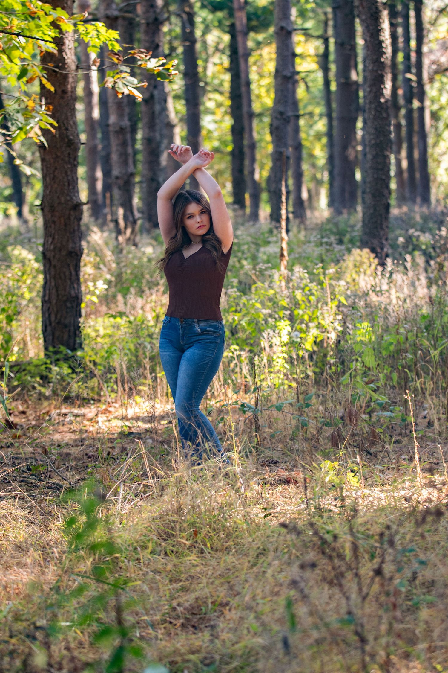 A person walking through a sunlit forest path wearing a brown top and jeans.