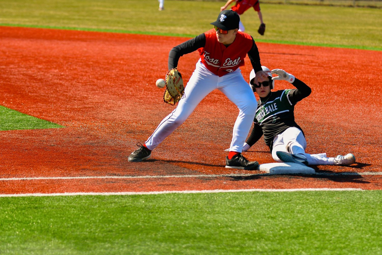 Baseball players sliding and fielding on a red dirt infield during game action.