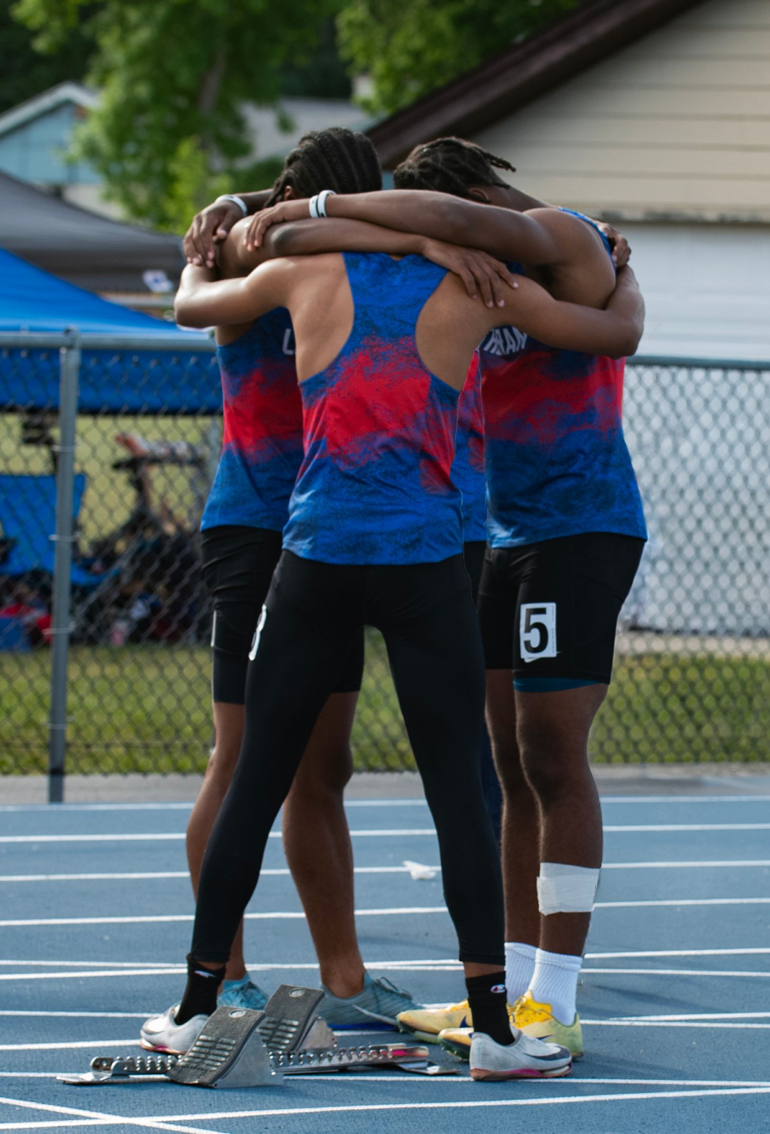 Track relay team in blue and red uniforms huddles together on the track before a race.