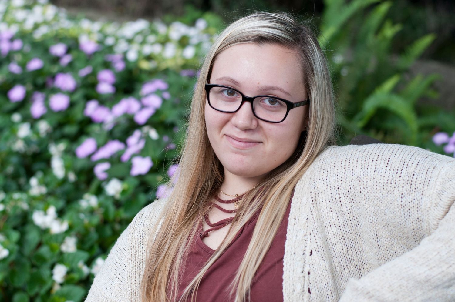 Portrait series of someone wearing glasses next to blooming pink flowers.