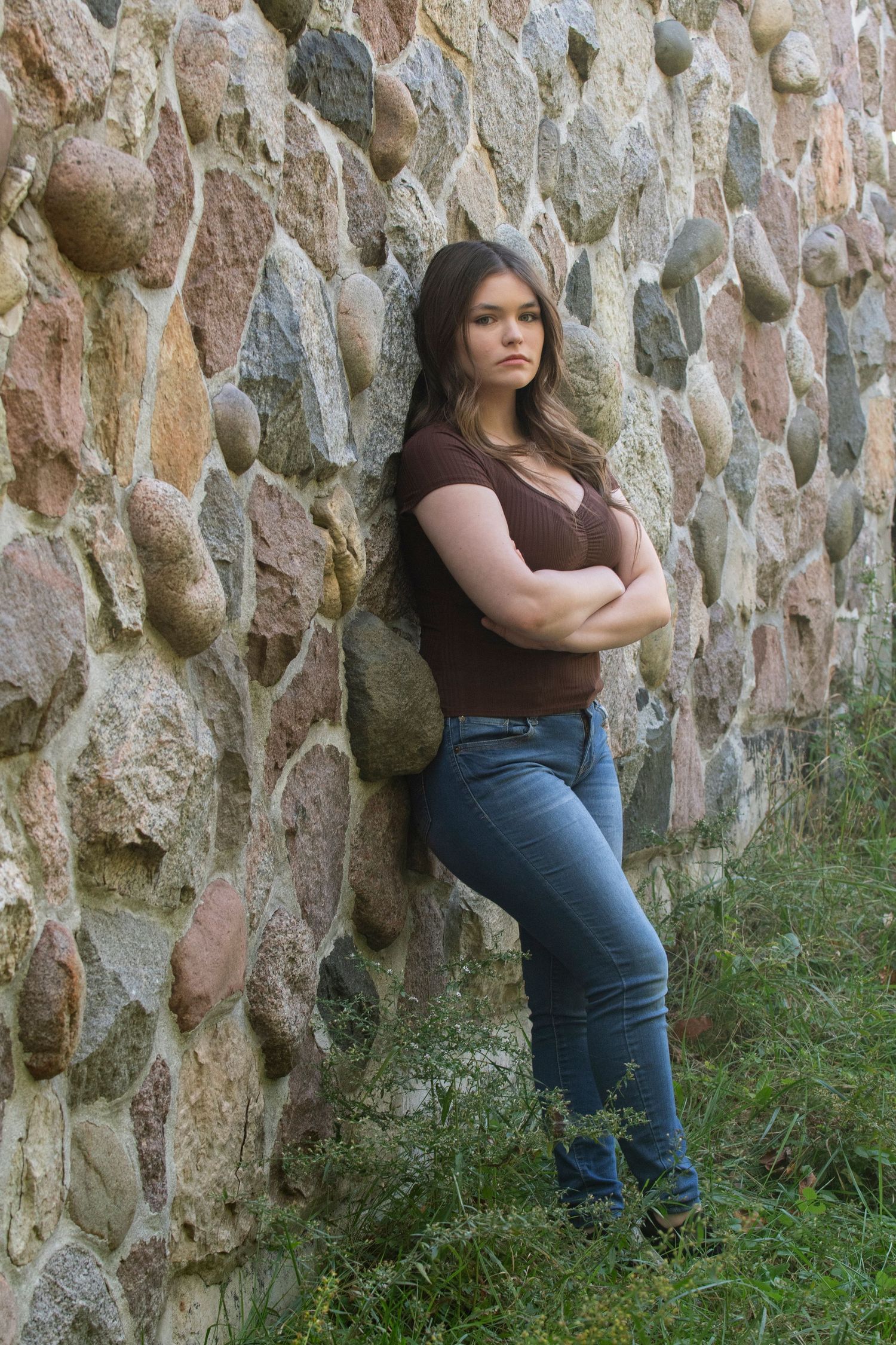 High school senior poses against rustic stone wall in the Kettle Moraine State Park in Delafield, WI for her Simply Junique Portrait Session