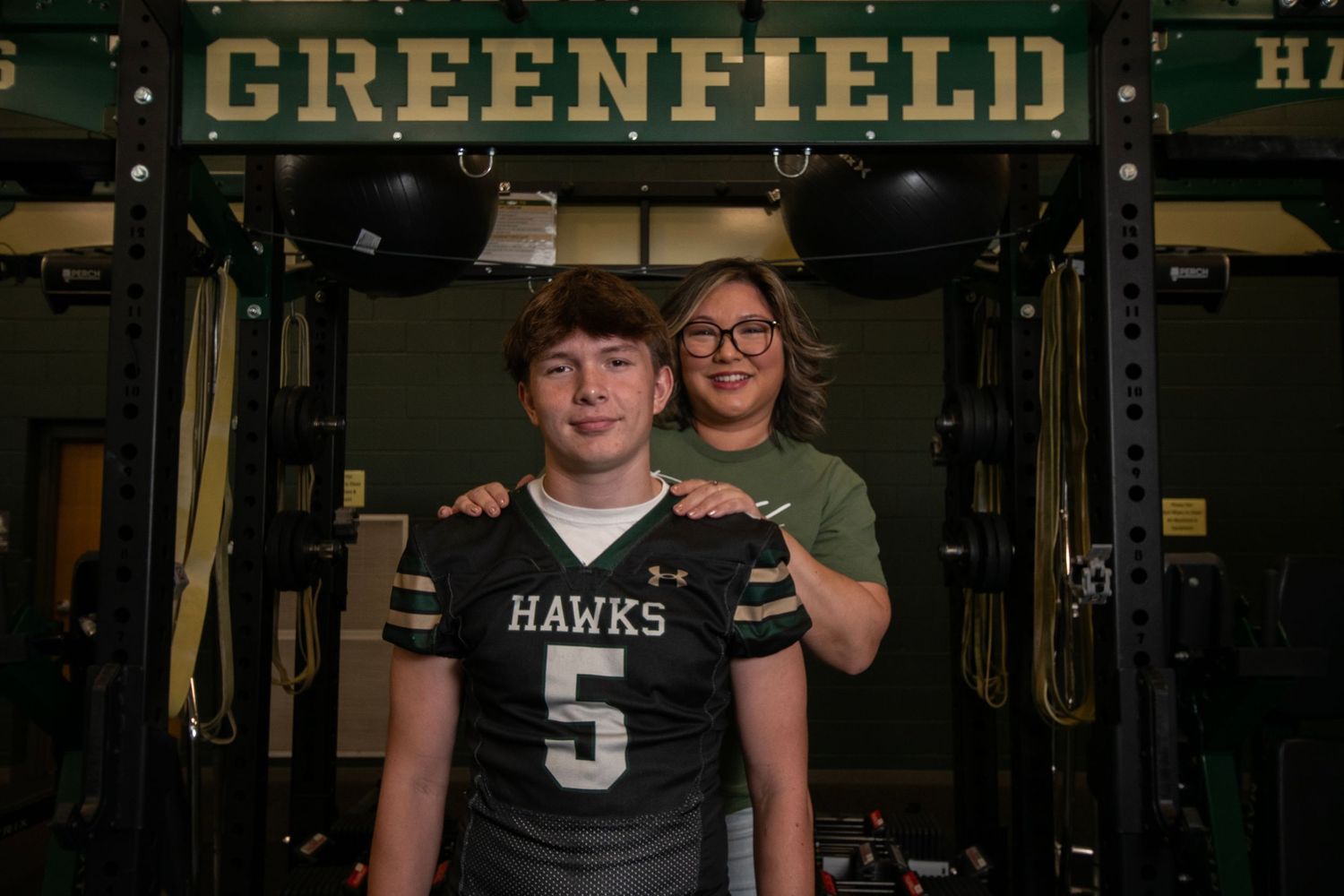 High school football players in black and green uniforms pose together in a dimly lit locker room or hallway.