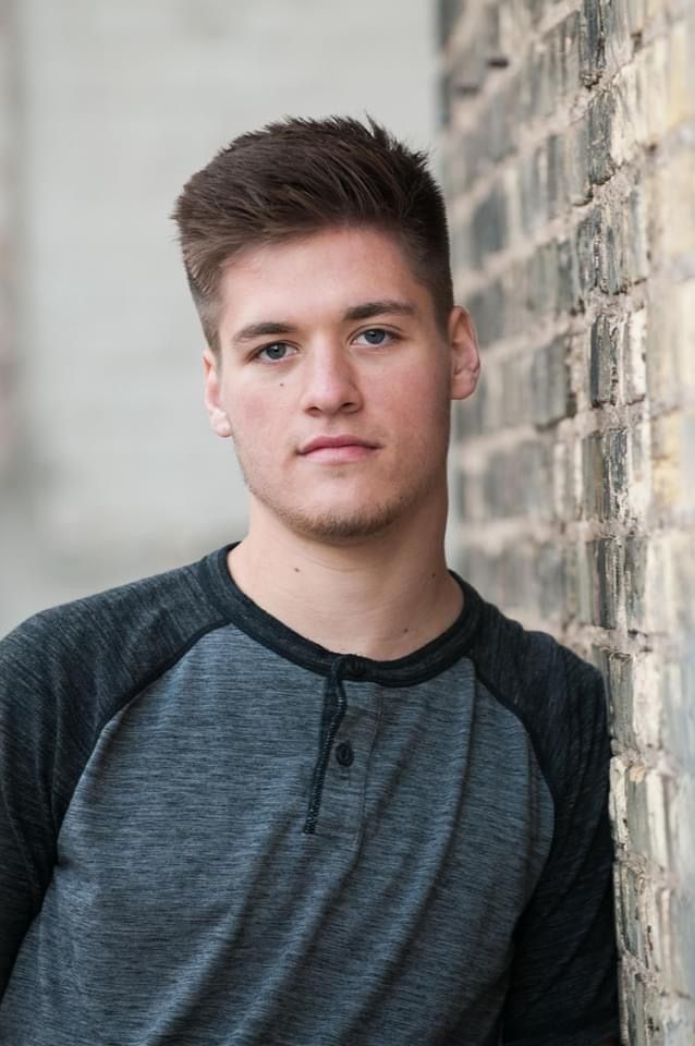 Portrait against textured brick wall wearing charcoal henley shirt.