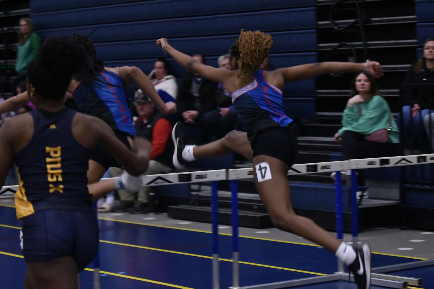 Track and field athletes competing in indoor meet with blue mats visible.