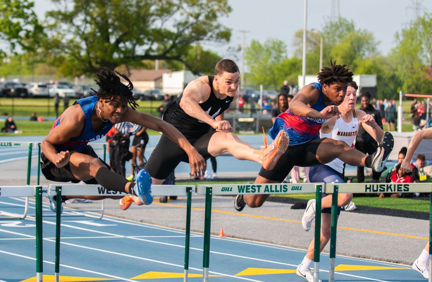 Athletes competing in a hurdles race on an outdoor track.