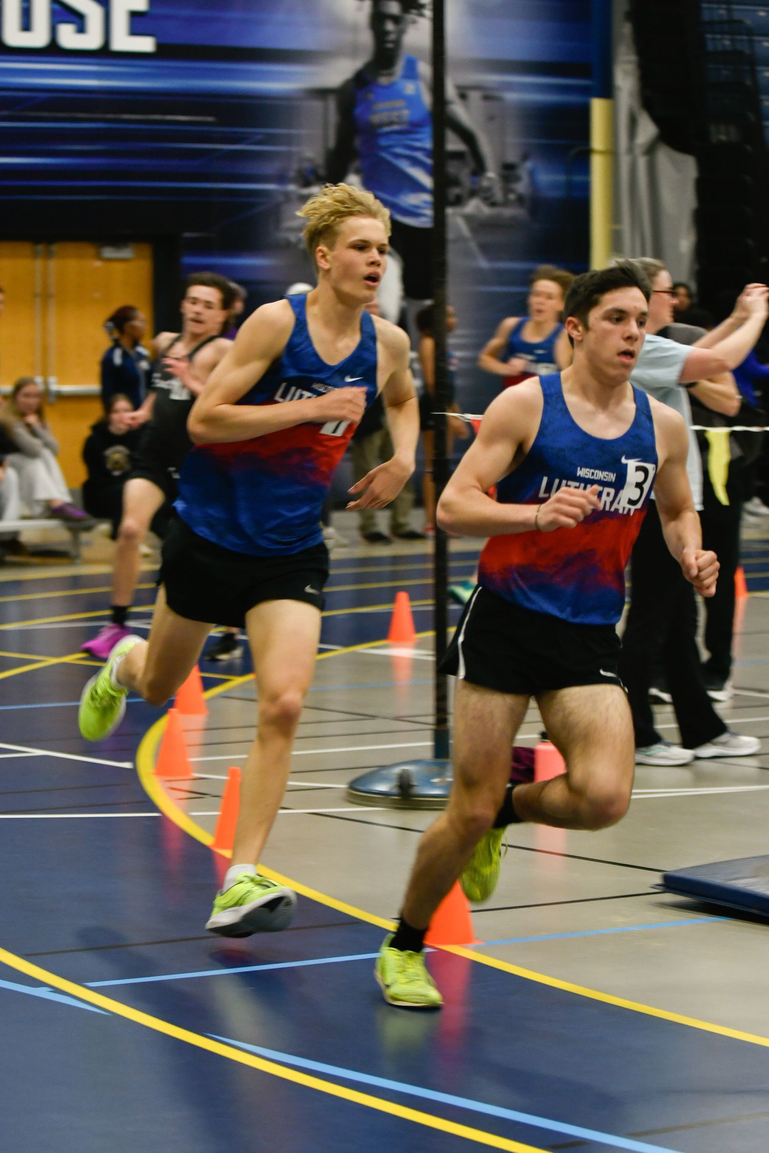 Track athletes sprint down a lane during an indoor competition with orange cones. Grounds Game Day to Grad Day Senior Portraits
