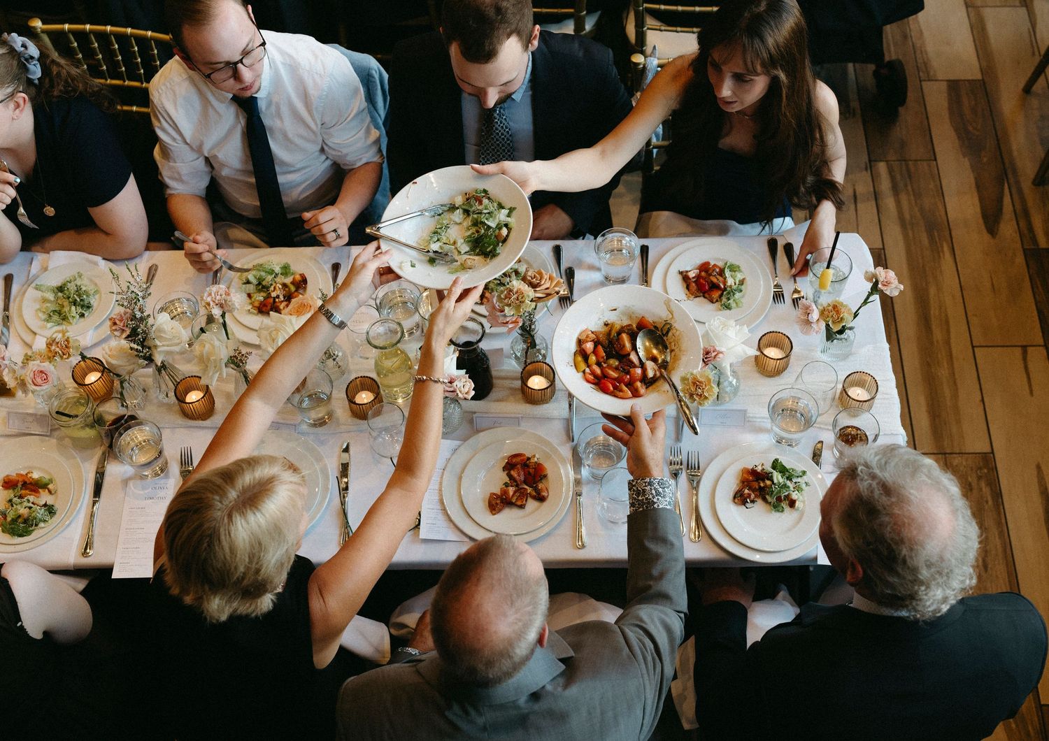 Overhead view of people dining together at a long wooden table with various plates of food.
