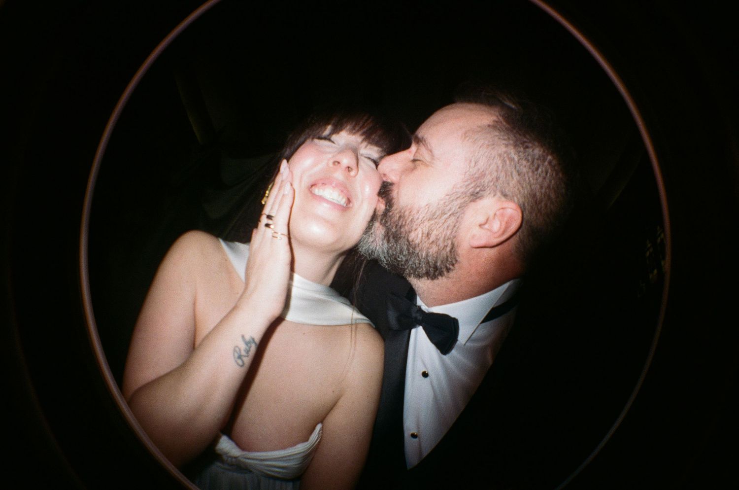 A couple in formal wedding attire share an intimate dance moment captured through a circular vignette frame.
