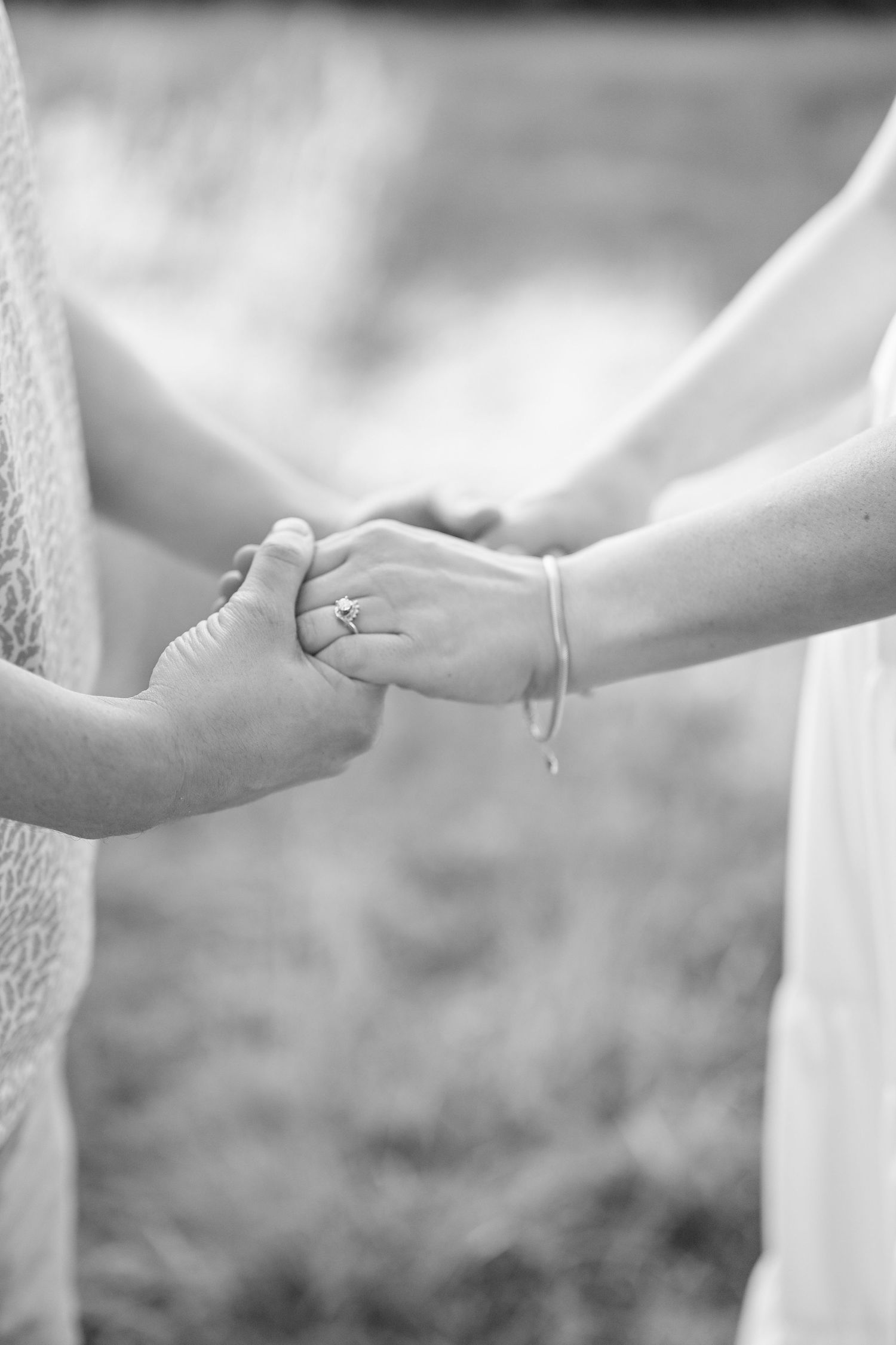 Black and white closeup of a couple's intertwined hands with the wedding ring visible on the woman's hand.