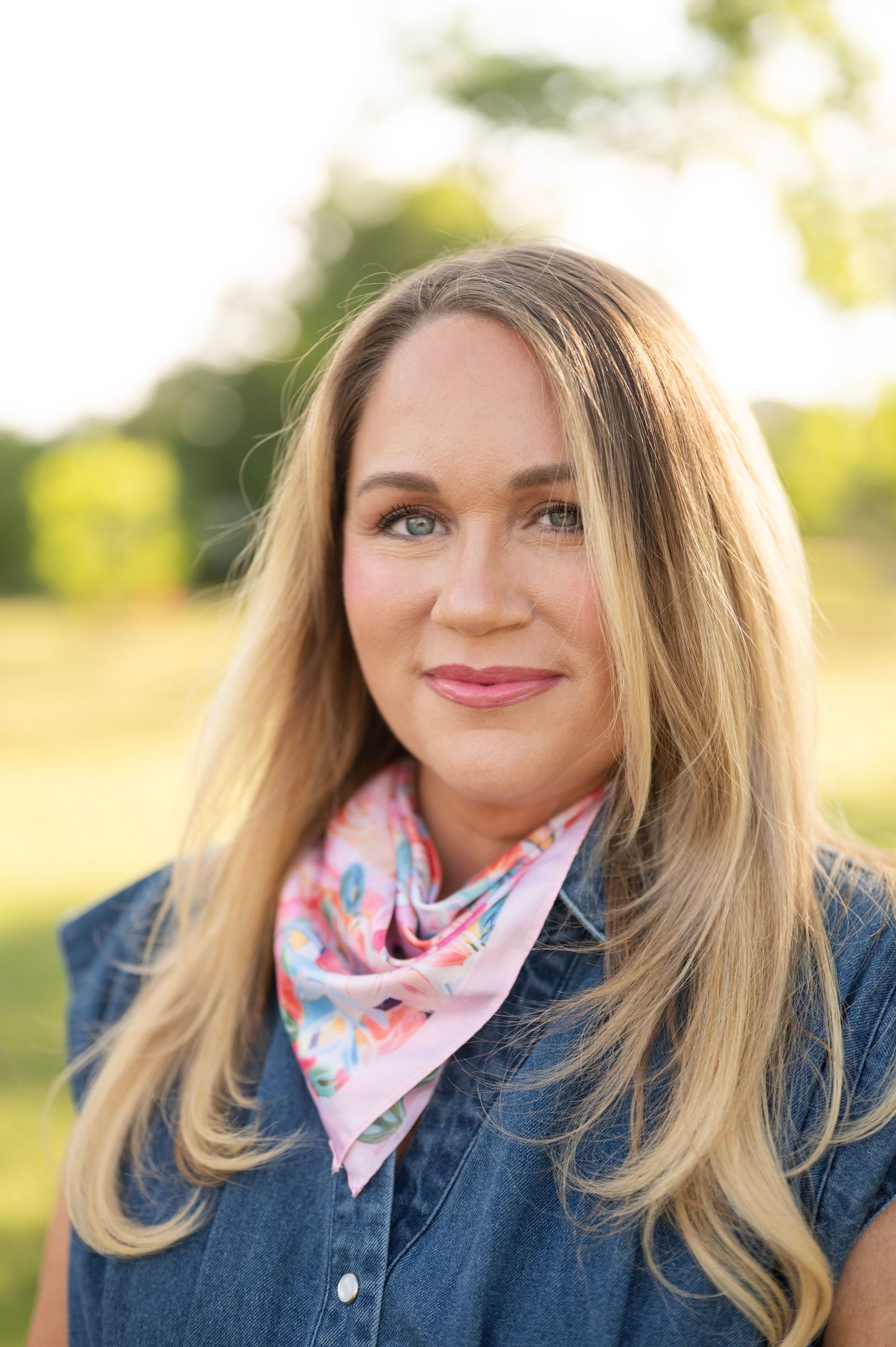 Portrait of a blonde woman in a pink floral bandana and denim jacket, shot outdoors in soft afternoon light.