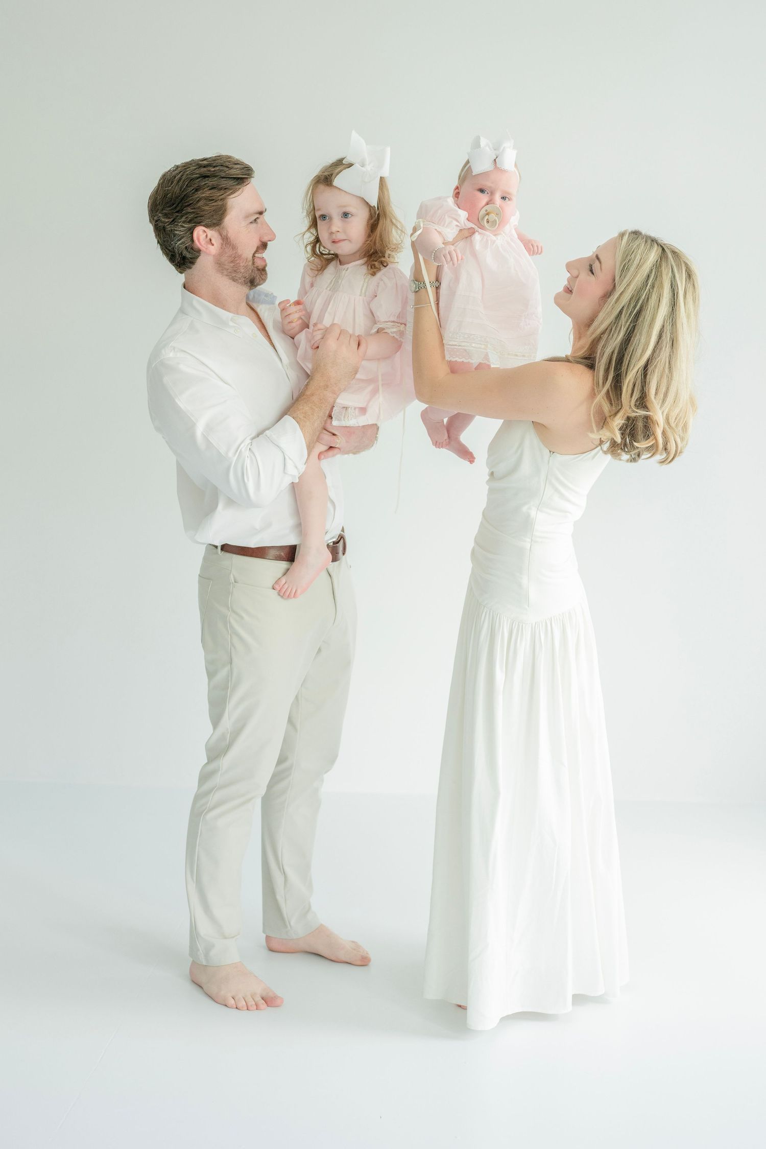 A family shares a joyful moment together wearing all white against a bright studio background.