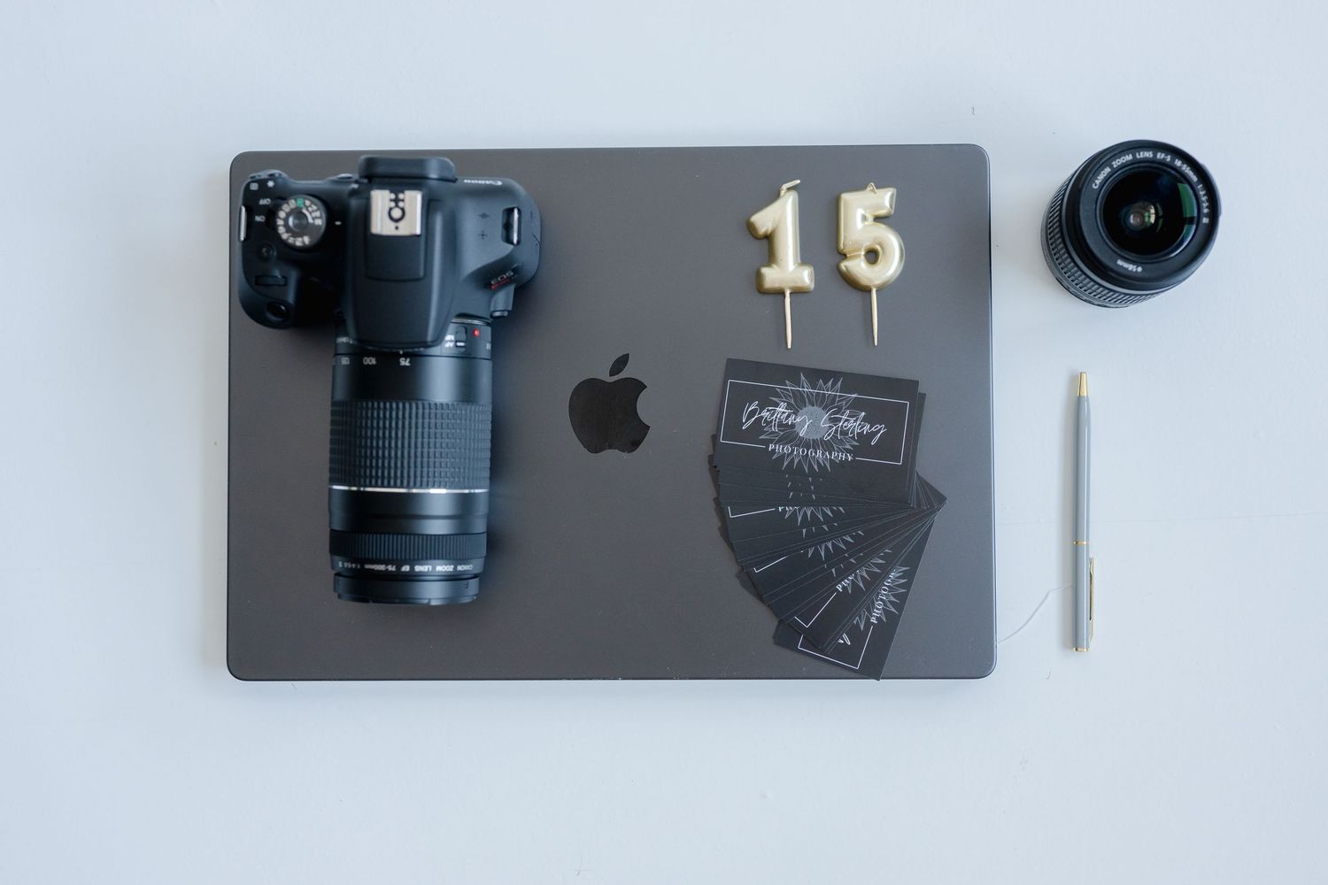 A collection of photography gear including camera lenses, MacBook, and Apple devices arranged neatly on a light surface.