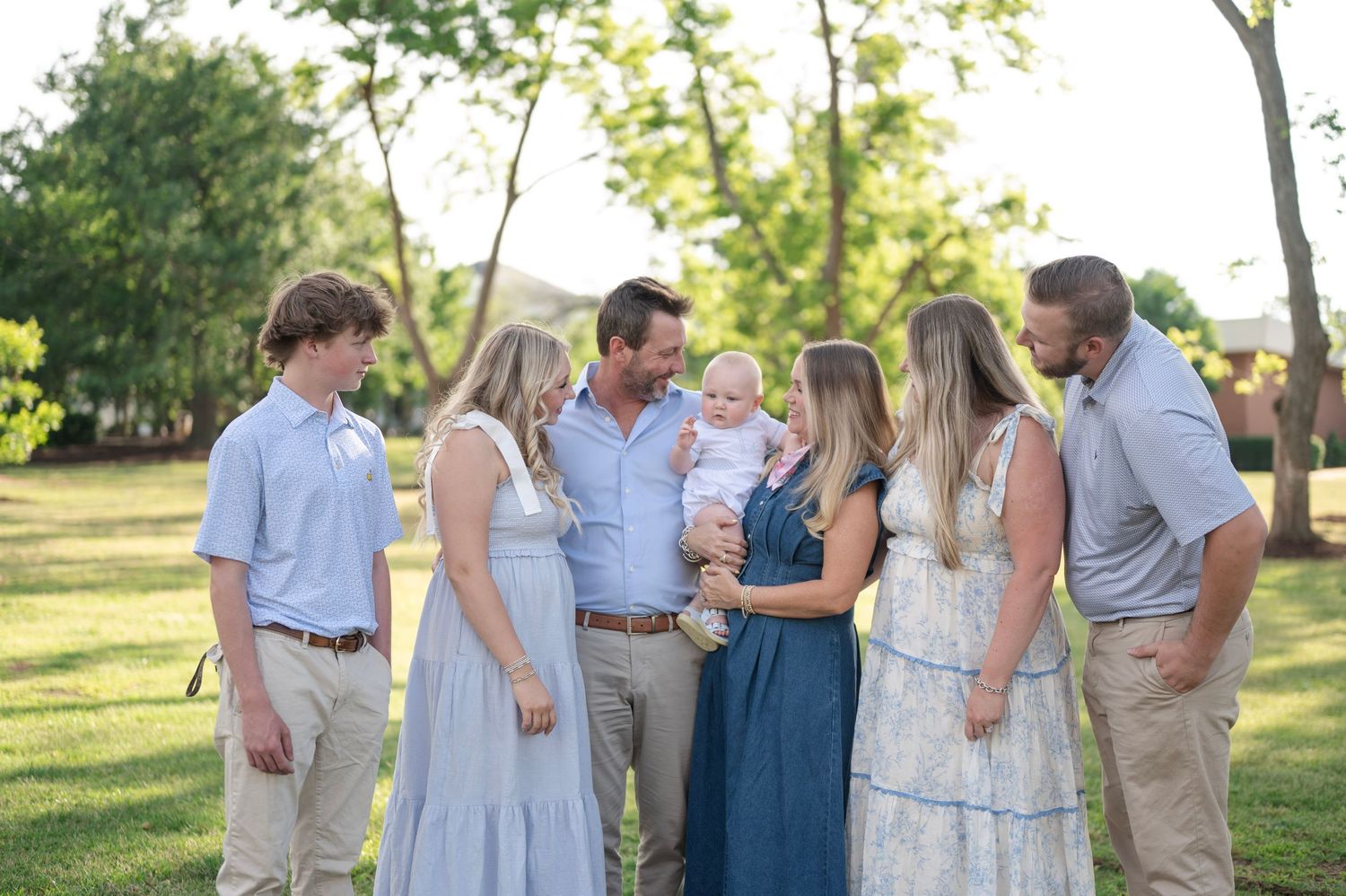 Family gathering outdoors in coordinated outfits sharing joyful moment in evening sunlight.